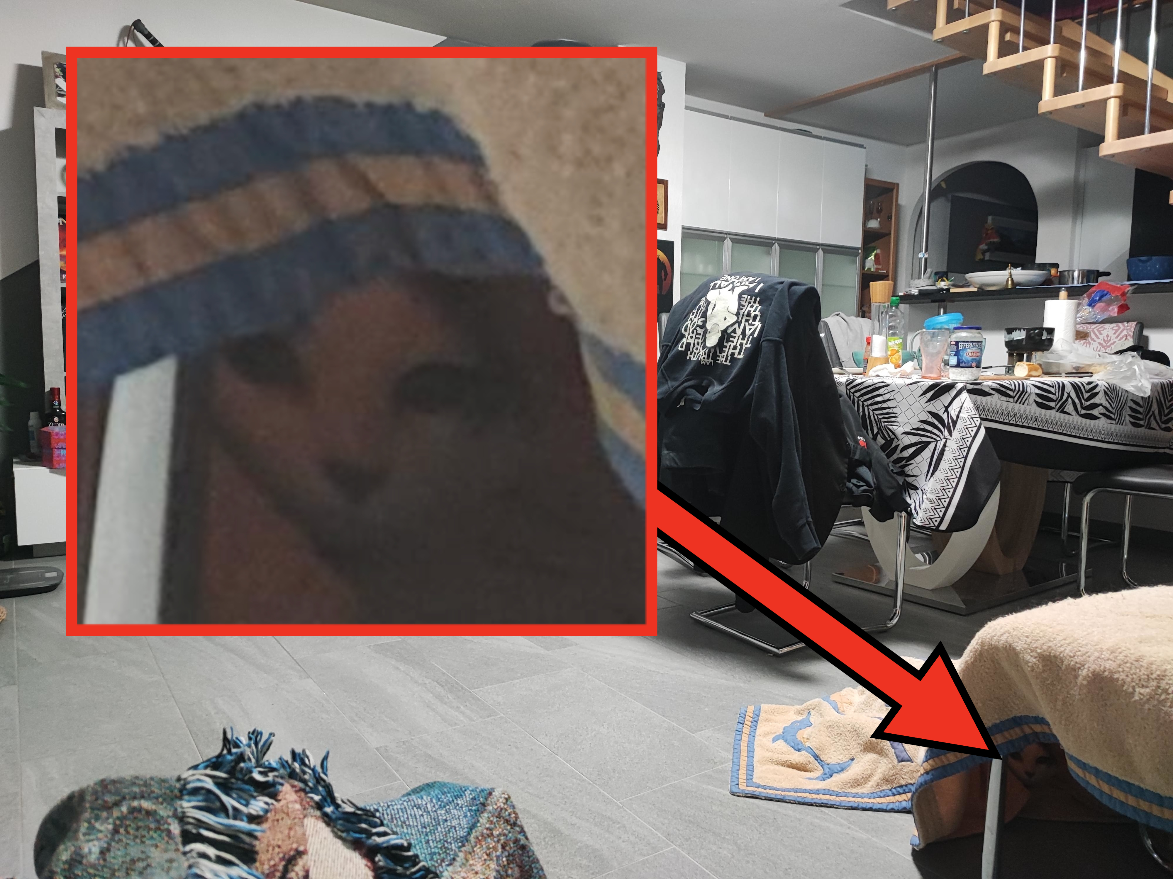 Living room with modern amenities, including a TV, a fireplace, shelves with various decorations, a dining table with chairs, and an overhead staircase