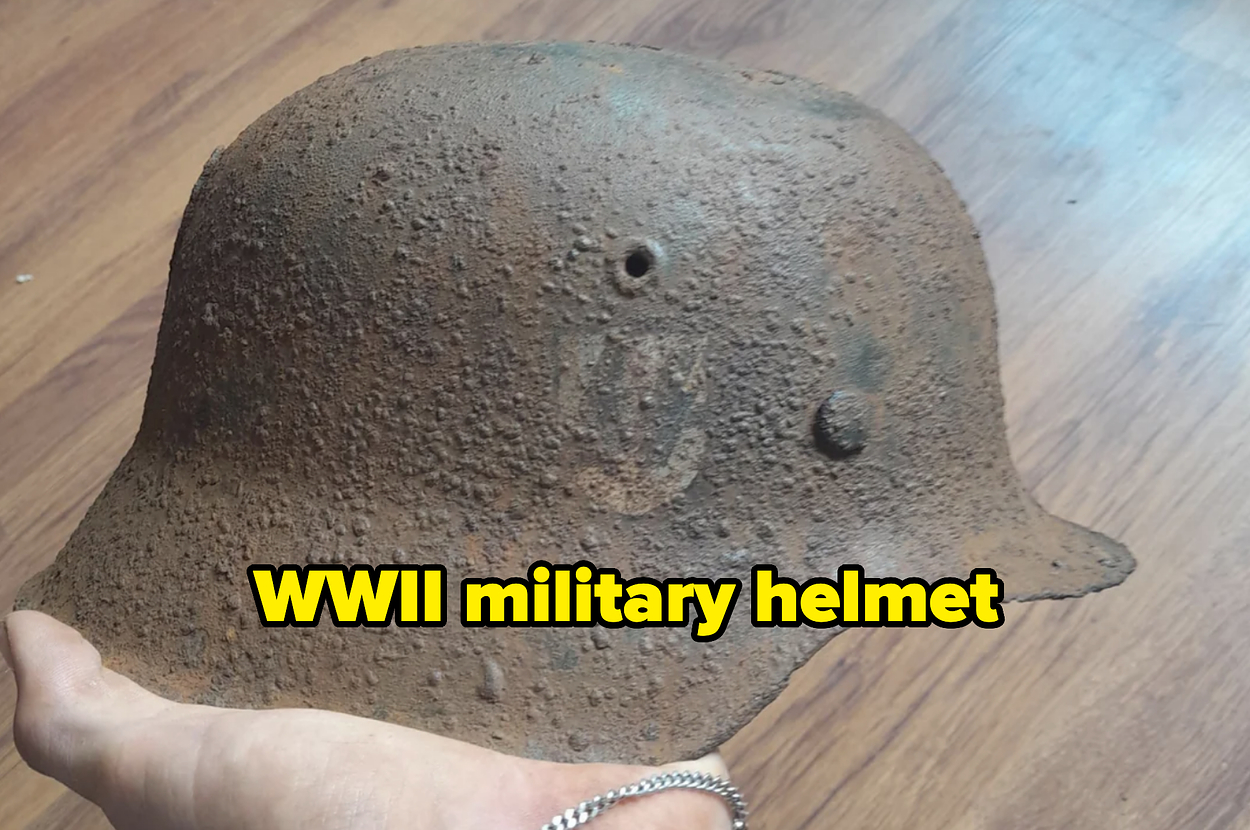 A rusted, old military helmet is held in the person's hand, showing significant wear and texture