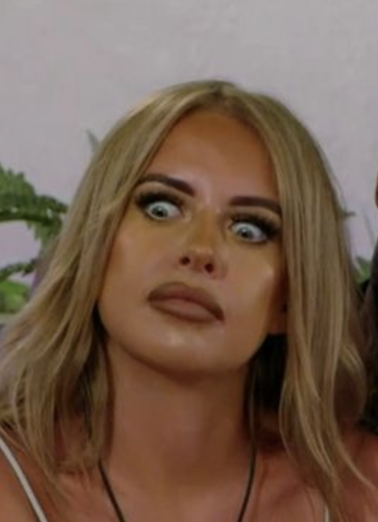 Close-up of a woman with wide-open eyes and an exaggerated, surprised expression on her face, wearing natural makeup and a casual top