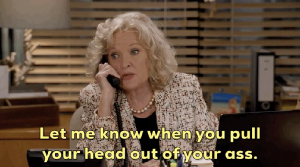A woman in an office talking on the phone. Text reads, "Let me know when you pull your head out of your ass."
