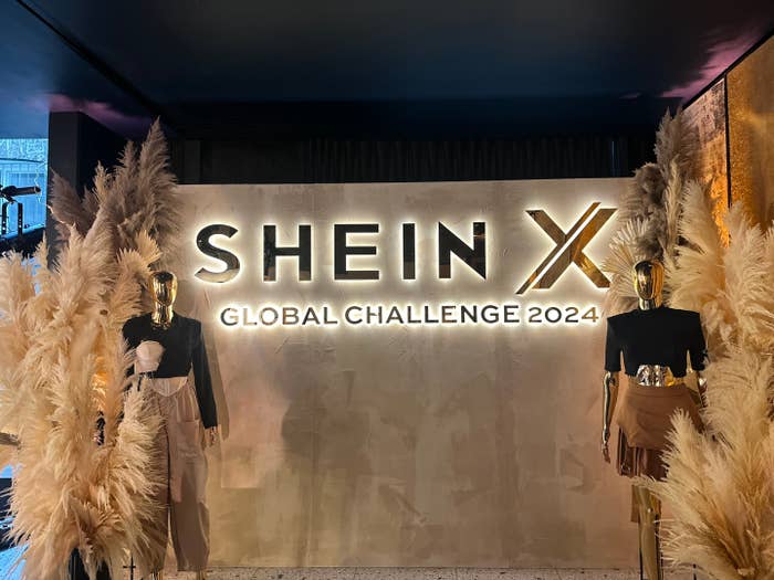 Shein X Global Challenge 2024 sign displayed with two mannequins wearing stylish black and beige outfits. The mannequins are surrounded by decorative pampas grass