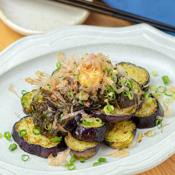 皿に盛り付けられた焼きナスの料理。削り節とネギがトッピングされている。