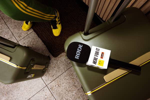 Microphone on a table beside a suitcase. Person in yellow sneakers and green pants with yellow stripes is partially visible