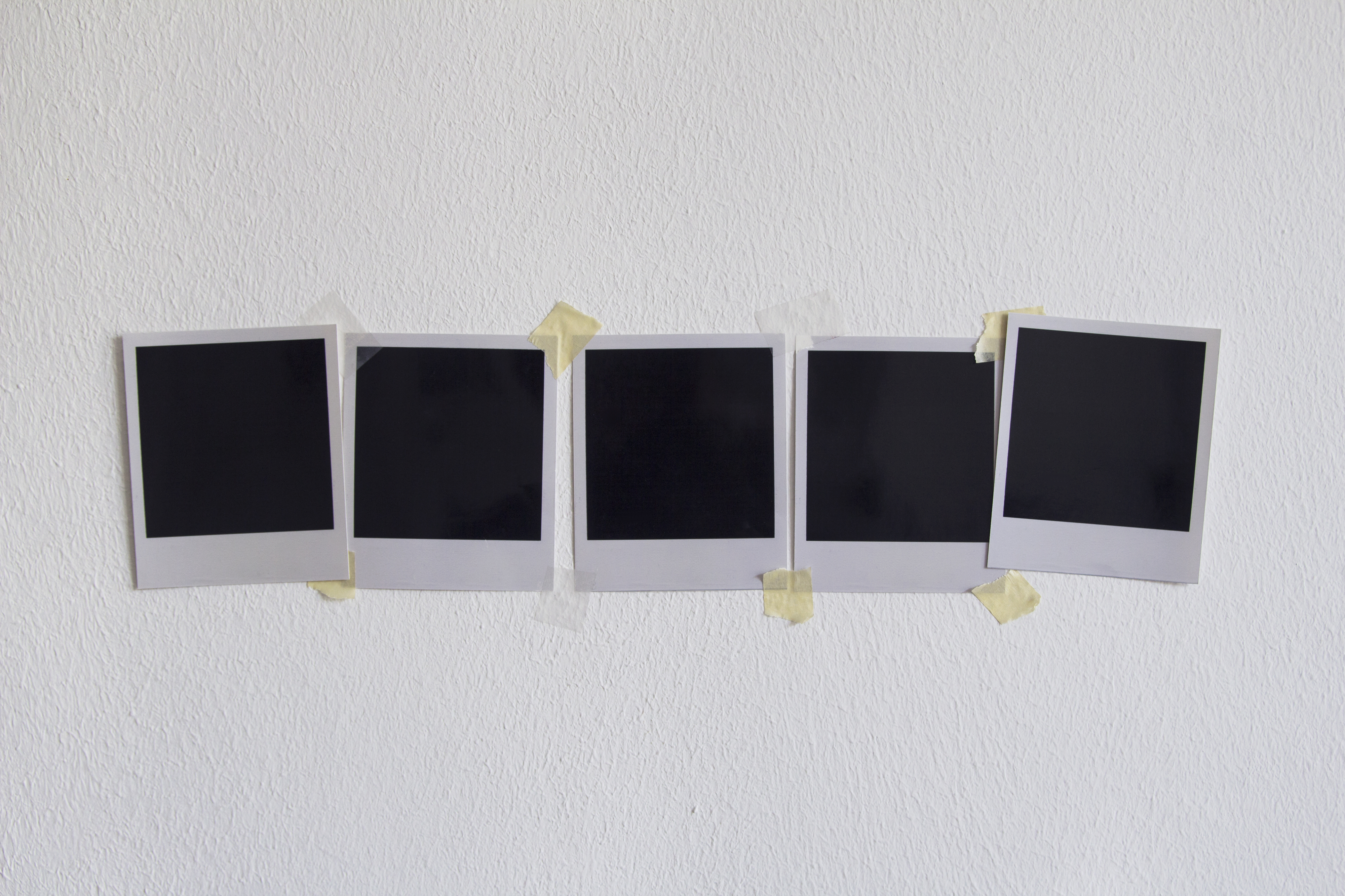 Five blank Polaroid photos are taped in a horizontal line on a textured wall