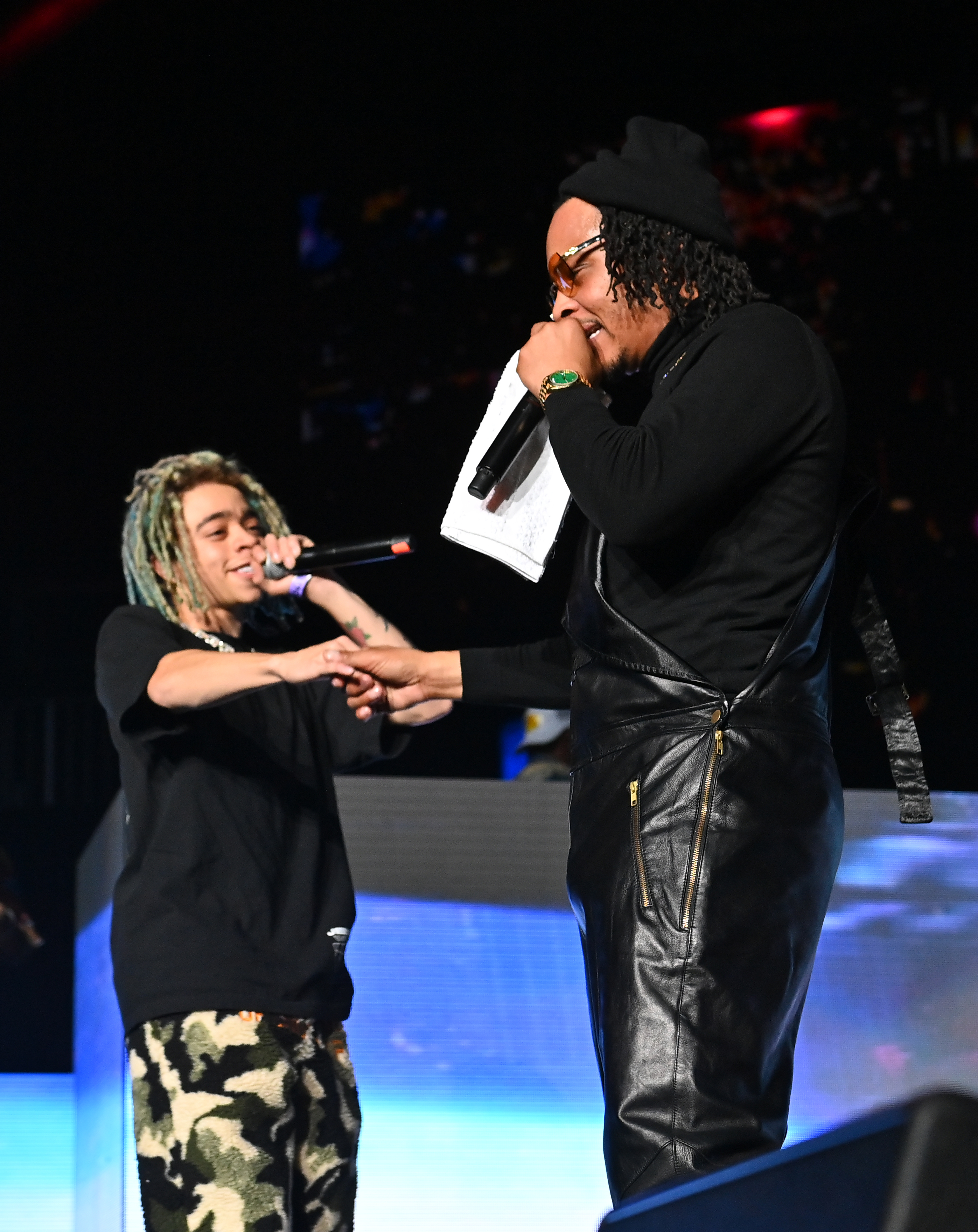 Lil Pump shaking hands with Ronny J on stage. Lil Pump wears a black t-shirt and camo pants; Ronny J is dressed in black leather overalls and a black beanie while holding a microphone