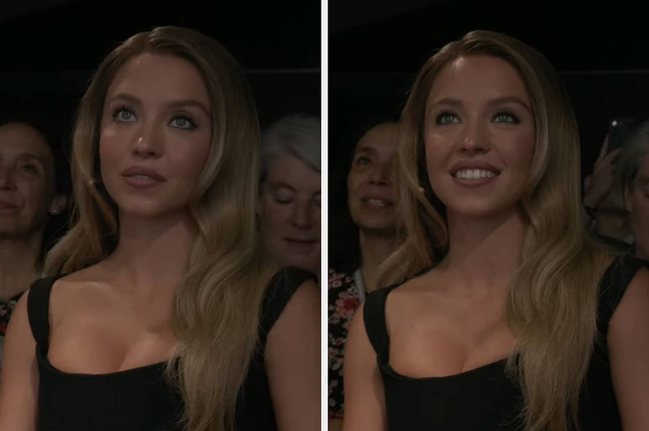 Sydney Sweeney smiles, wearing a casual black top, in a studio setting with a blurred background