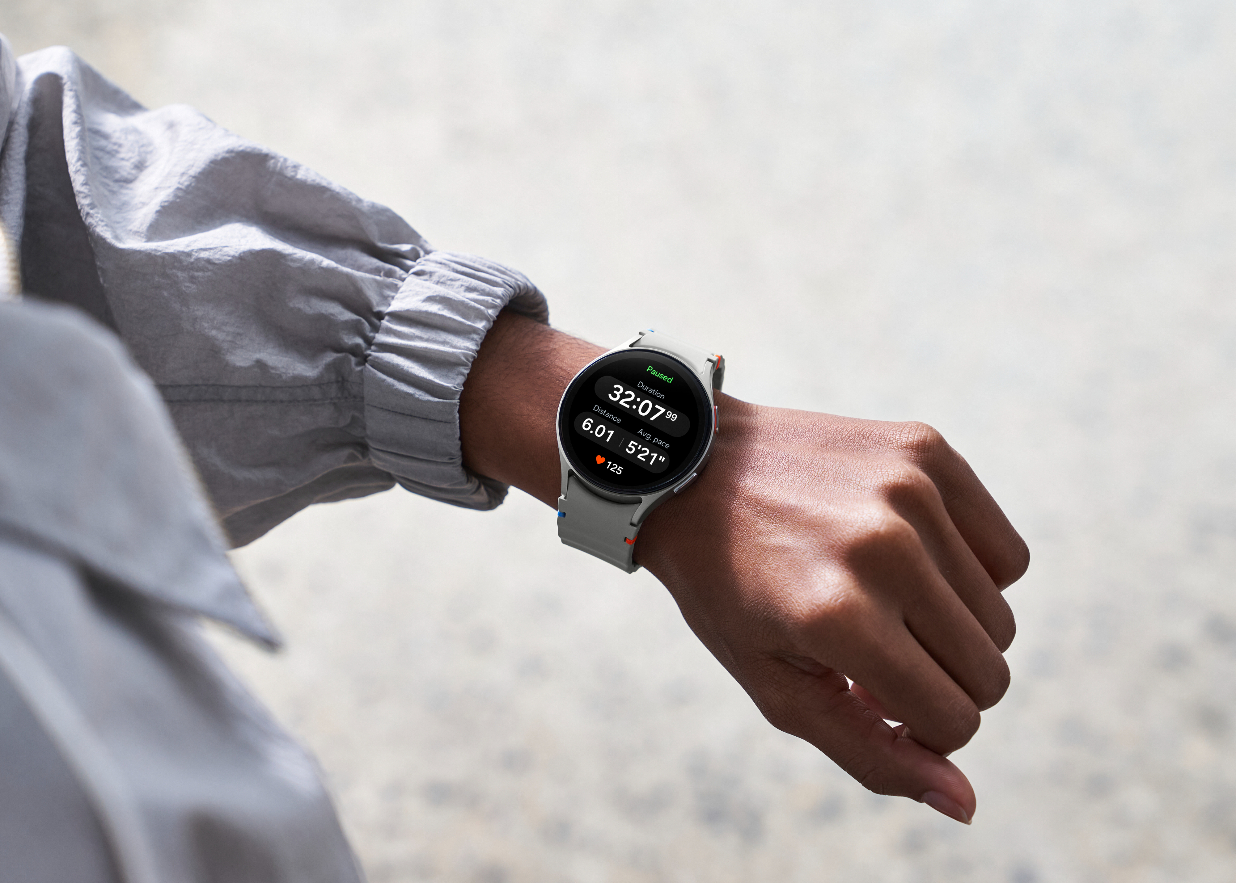 A close-up of a person's wrist wearing a sleek smartwatch displaying the time, date, heart rate, and step count. The person is wearing a long-sleeve shirt