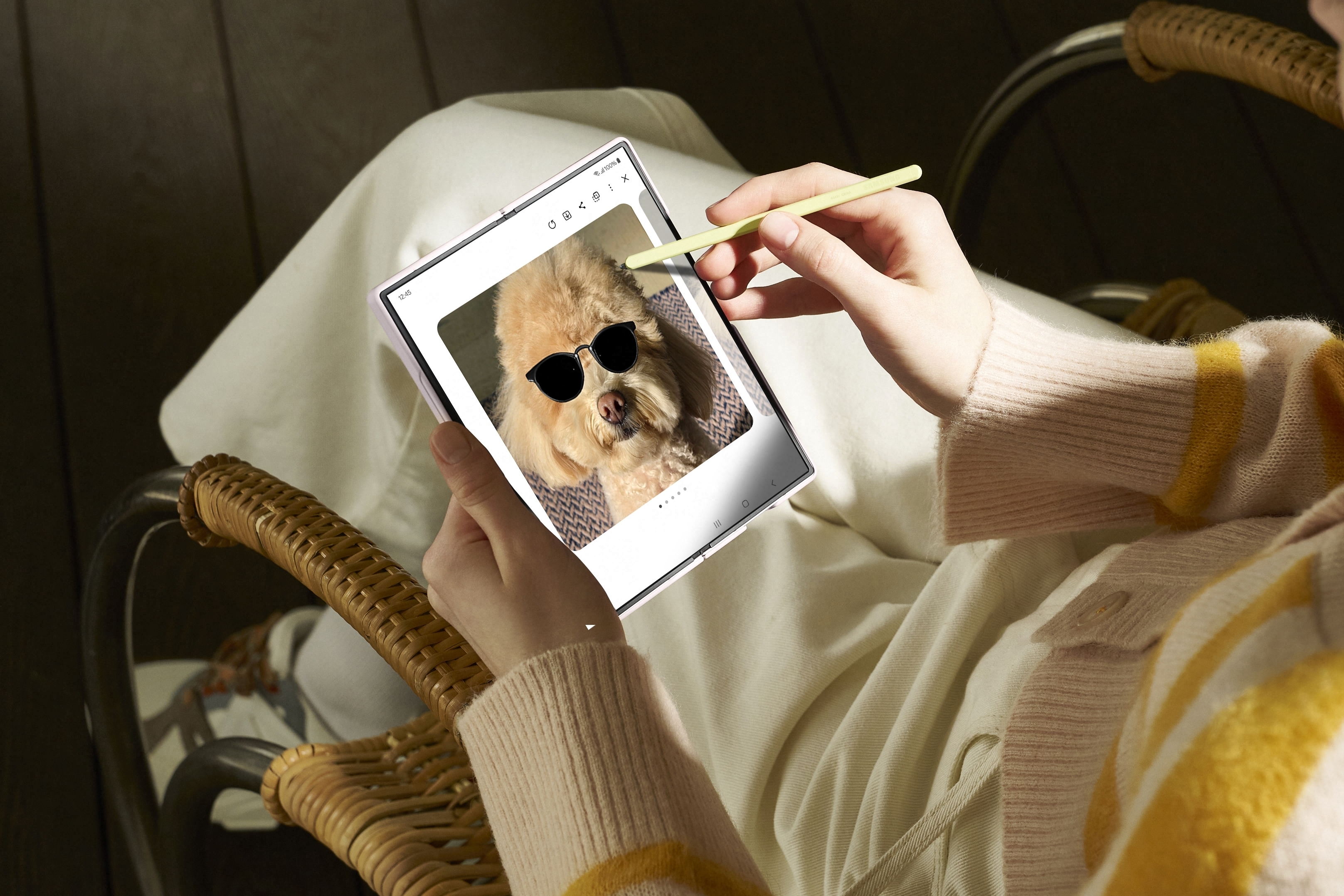 A person is using a stylus to edit a photo of a dog wearing sunglasses on a foldable tablet