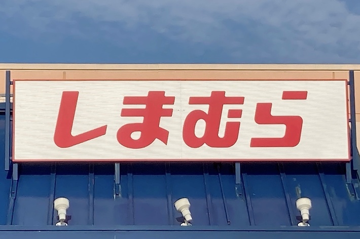 A storefront with a sign in Japanese katakana characters that reads &ldquo;Shimamura.&rdquo; The foreground shows an accessible parking sign