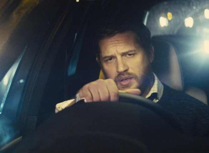 Tom Hardy is driving a car at night, focused on the road ahead