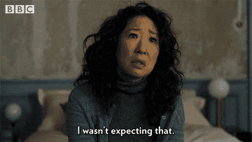 Sandra Oh, looking surprised, says "I wasn't expecting that" in this scene from a BBC show. She is wearing a cardigan over a turtleneck