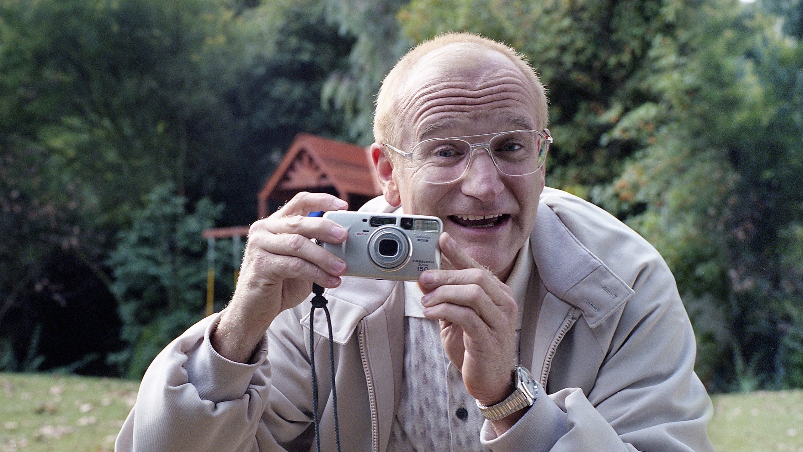 A smiling person holds a camera while outdoors