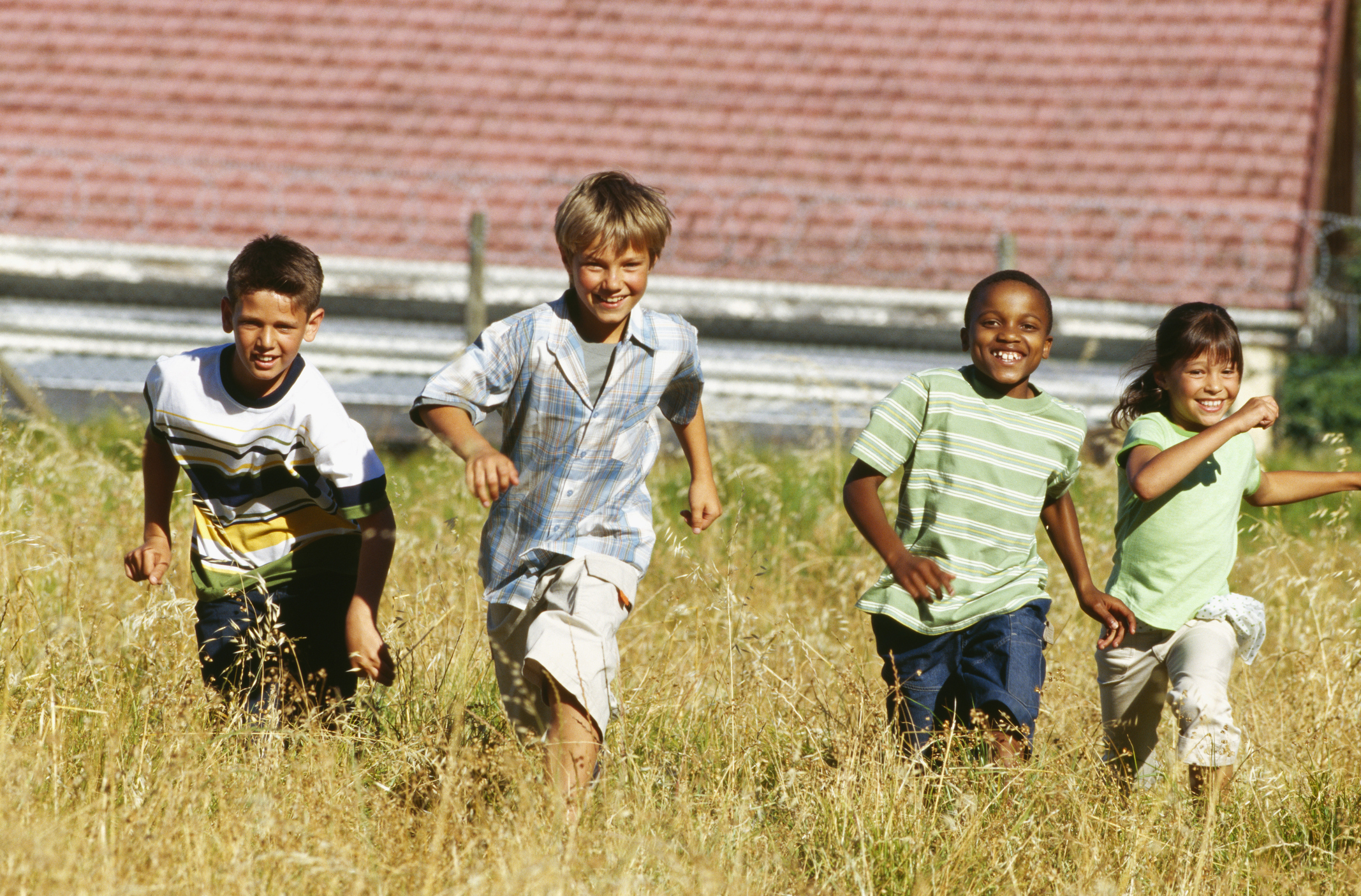 A group of four children, two boys and two girls, are running through a grassy field, smiling and enjoying themselves