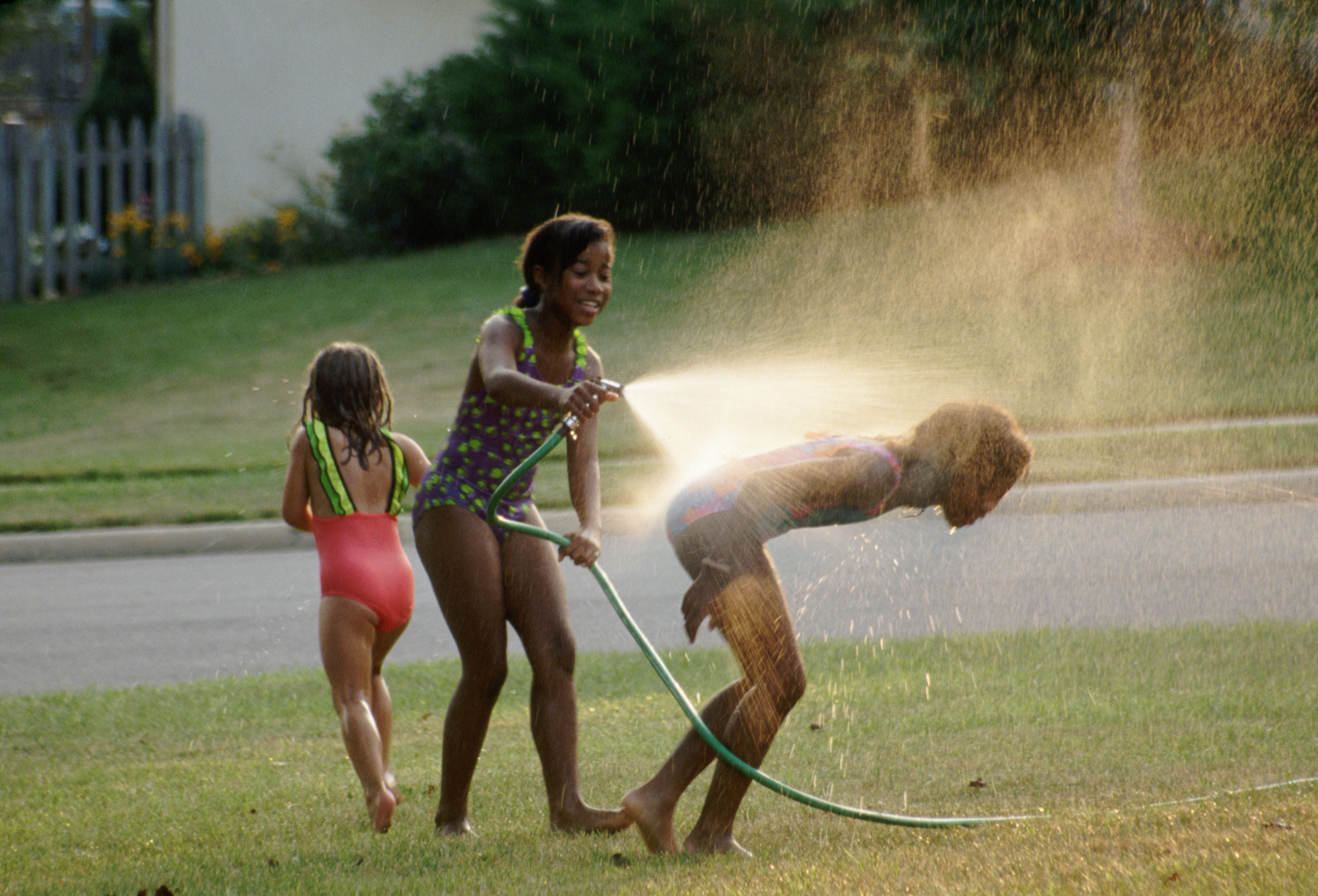 Three children play with a garden hose in a yard, spraying water and enjoying a summer day