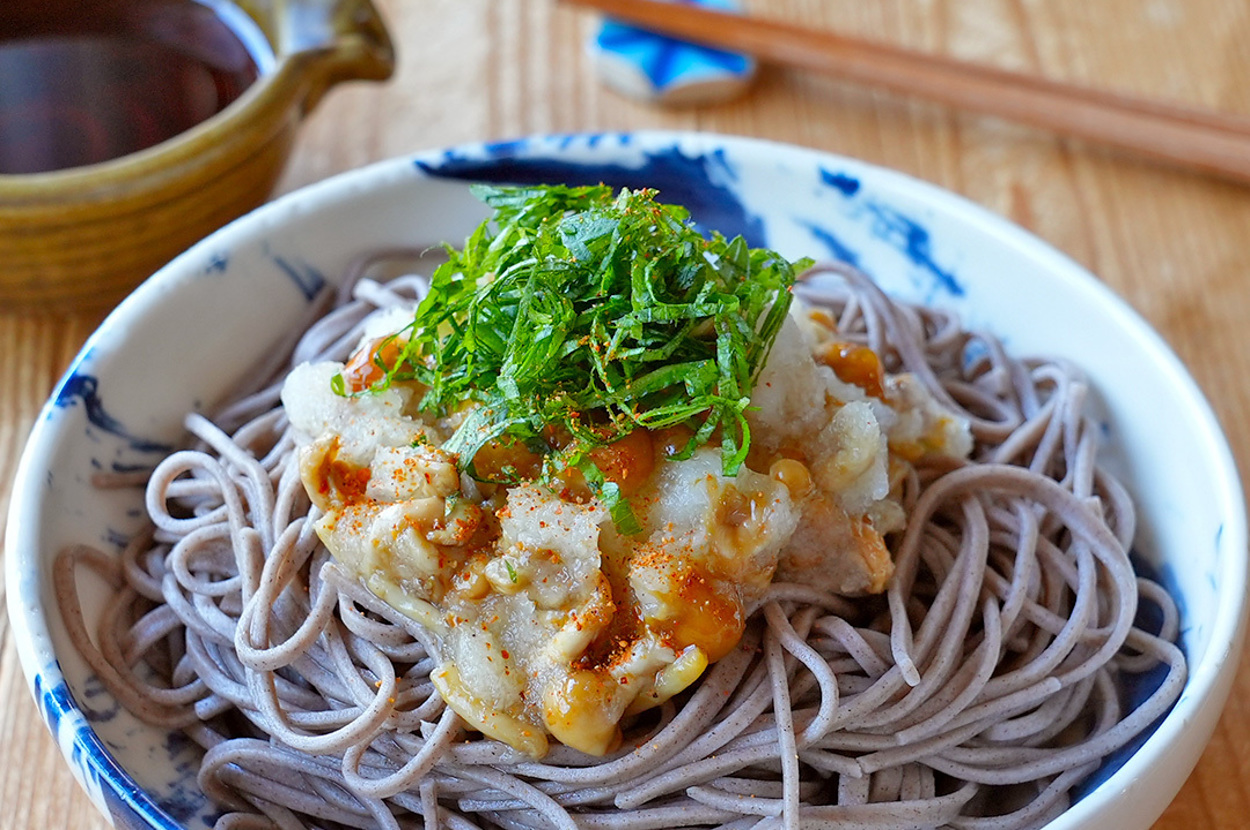 そばの器に盛り付けられたそばの上に、薬味と具材がのっている。そばつゆと箸も見える。