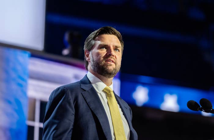 J.D. Vance stands at a podium, wearing a suit and tie, addressing an audience