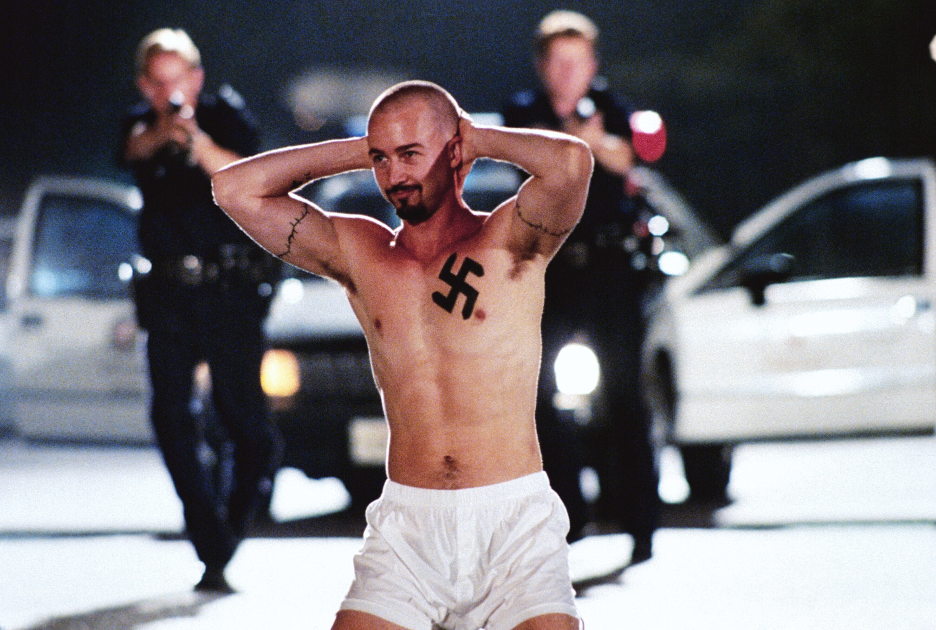 Edward Norton in American History X with a swastika tattoo on his chest is being arrested by police officers pointing guns at him