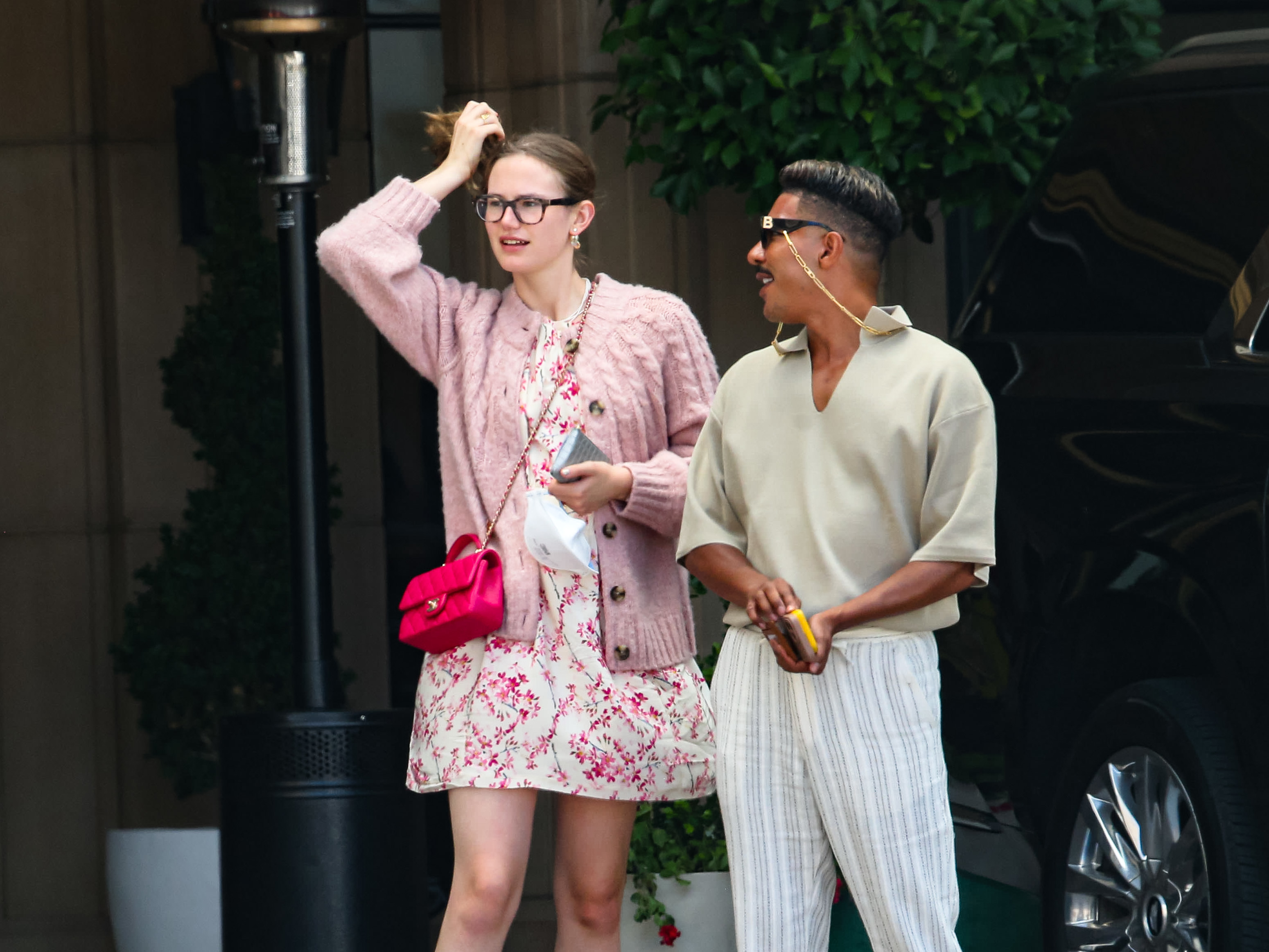 Don't know who they are. Woman in a floral dress and cardigan with a red purse and glasses. Man in a beige shirt and striped pants with sunglasses and earphones
