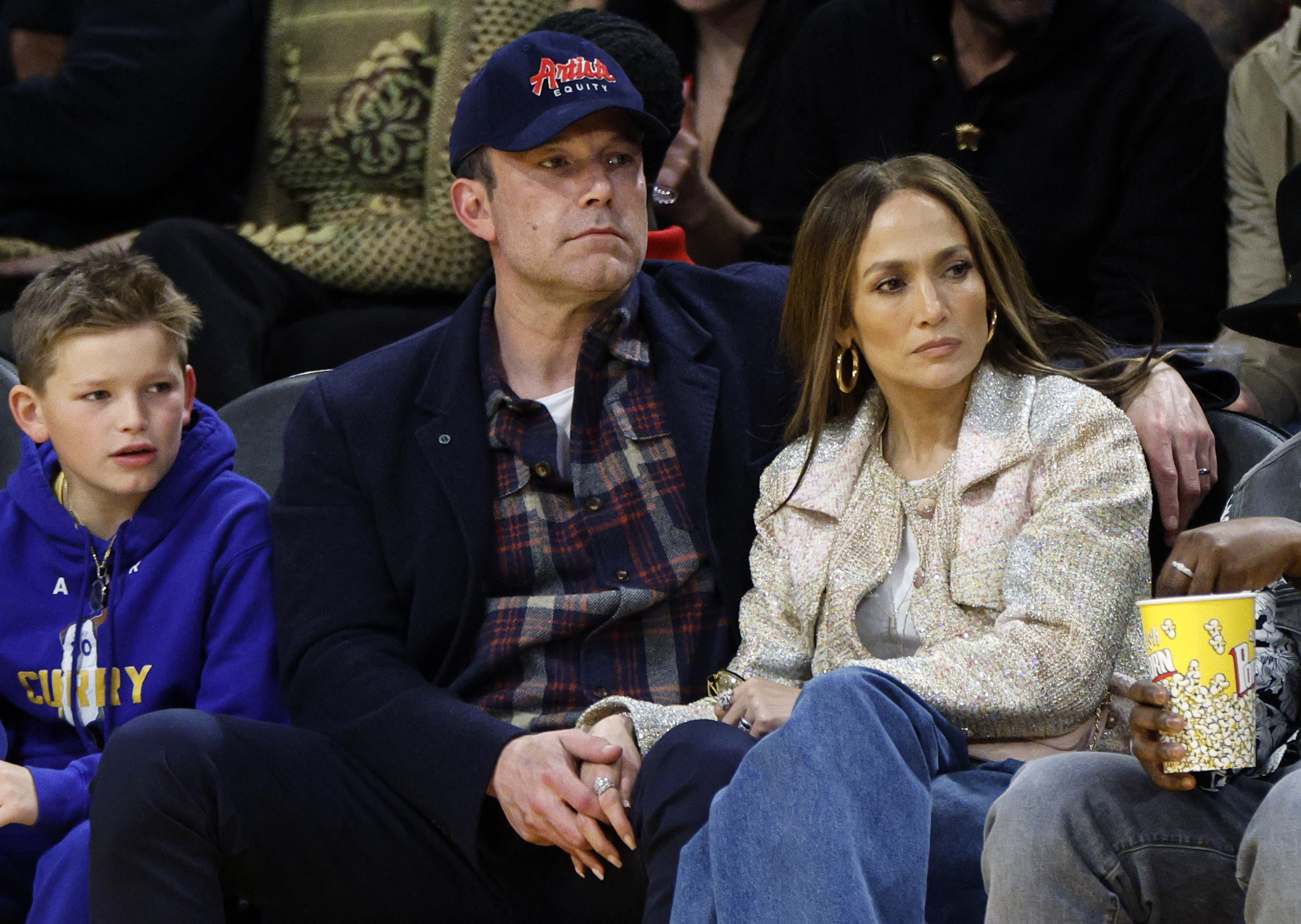 Sam Affleck, Ben Affleck, and Jennifer Lopez sit courtside at a basketball game, holding hands