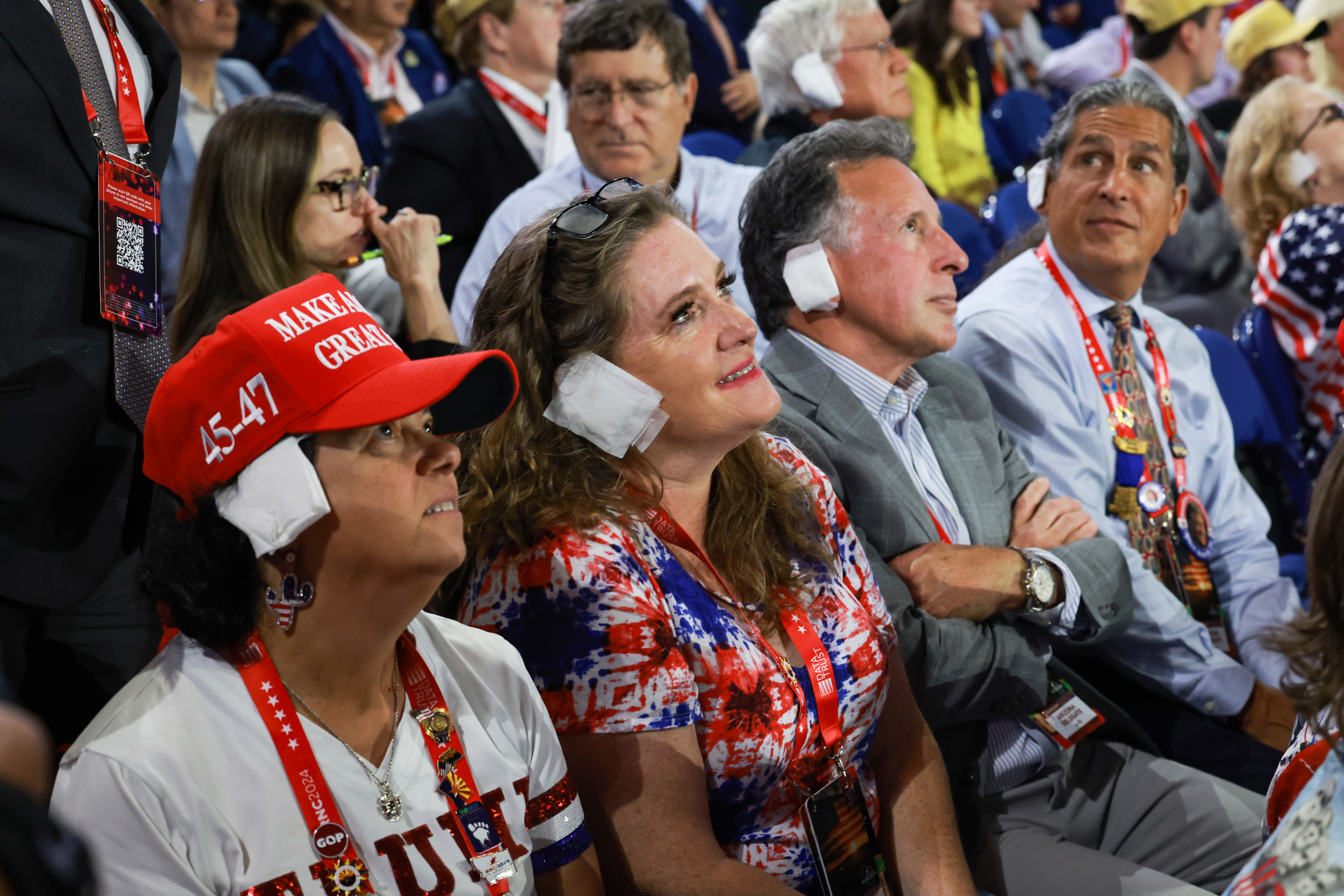 People at an event wearing earplugs, including a woman in a &quot;Make America Great Again&quot; hat and a red-white-blue t-shirt. Audience members in the background