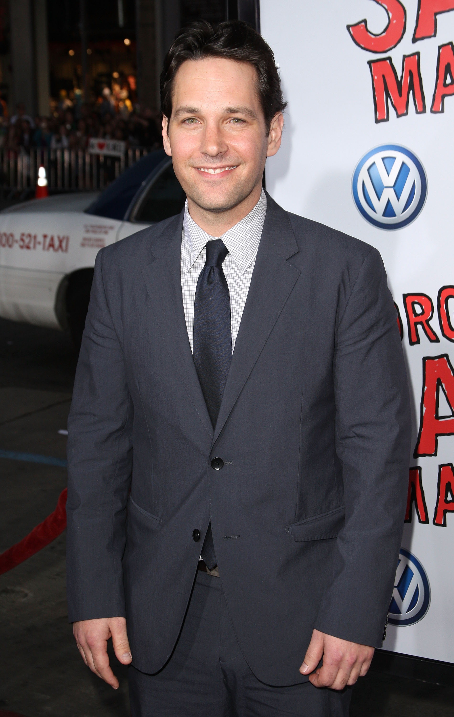 Paul Rudd at a red carpet event, wearing a dark suit with a tie, smiling for the camera