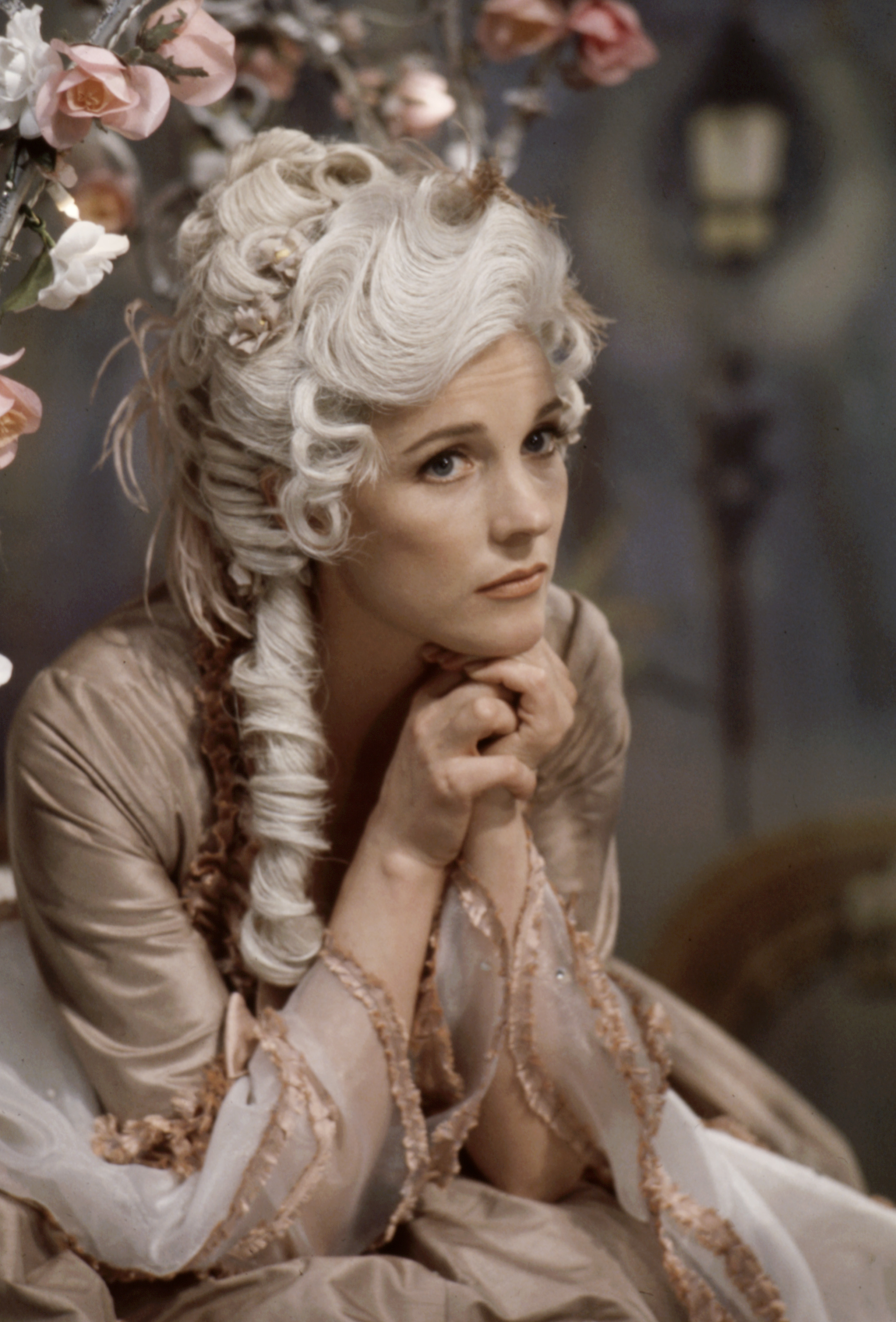 Actress in a Marie Antoinette-inspired costume with elaborate wig and period dress, posing with hands clasped under chin