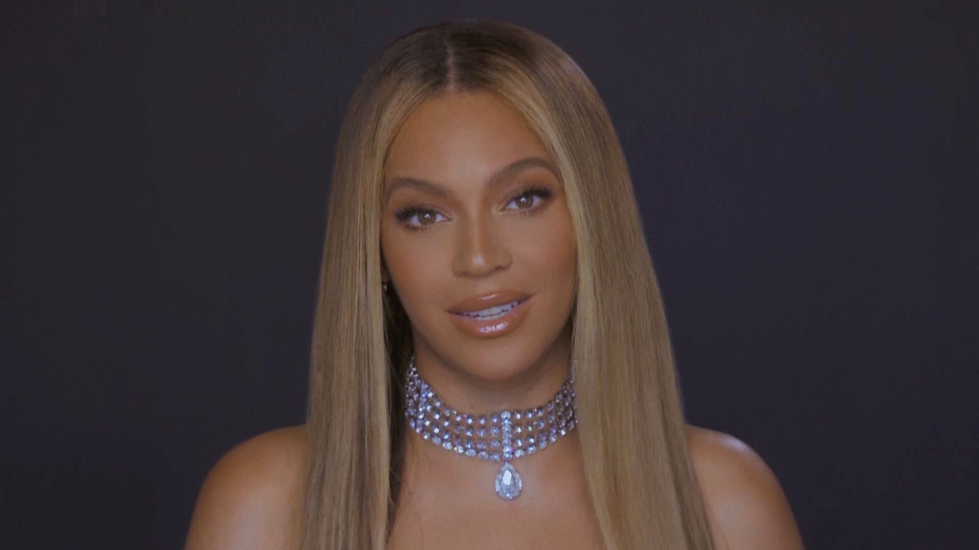 Beyoncé looking directly at the camera, wearing a strapless top and a sparkly choker necklace with a large gemstone pendant