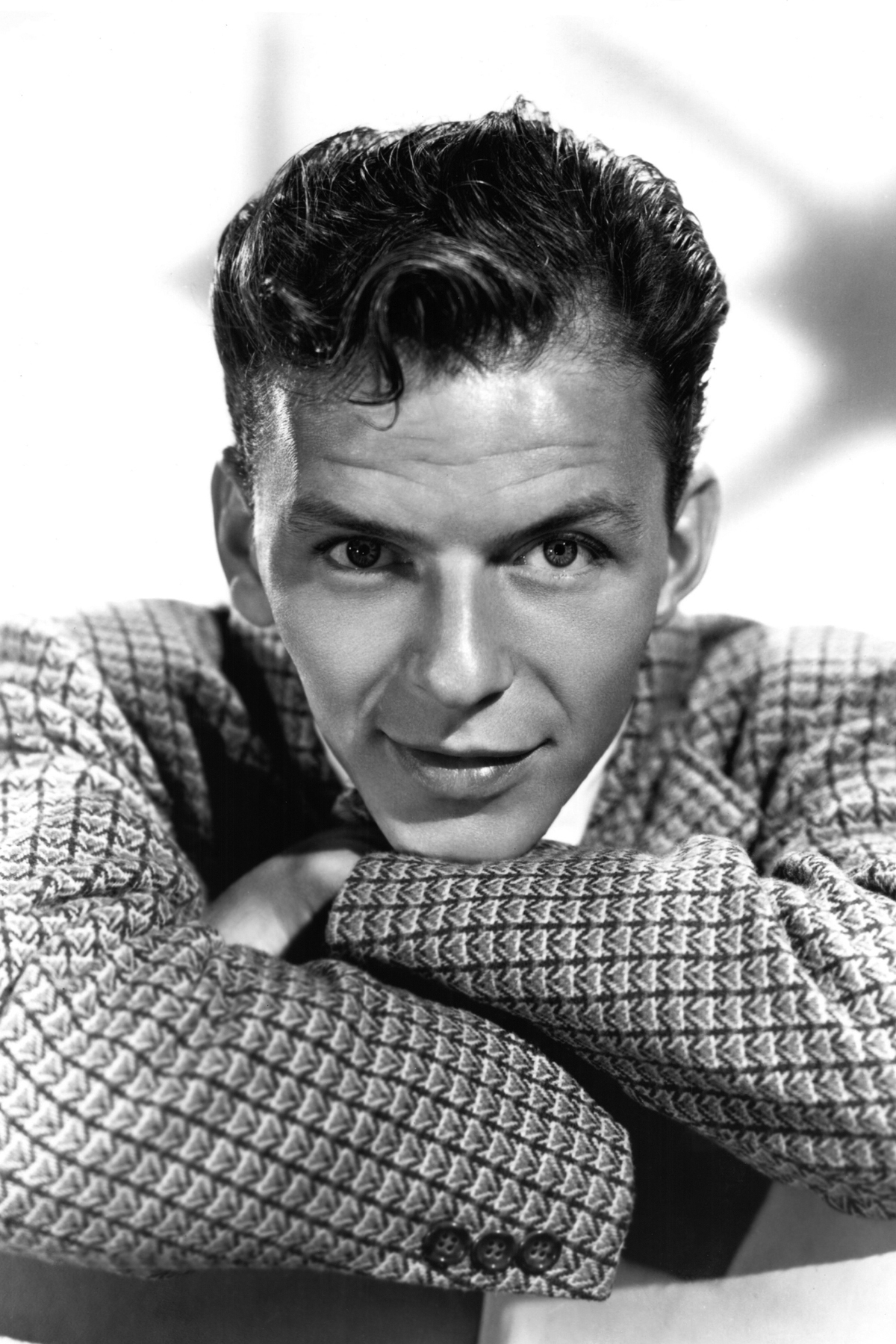 Frank Sinatra, in a checkered suit, leans forward with his arms crossed, looking directly at the camera