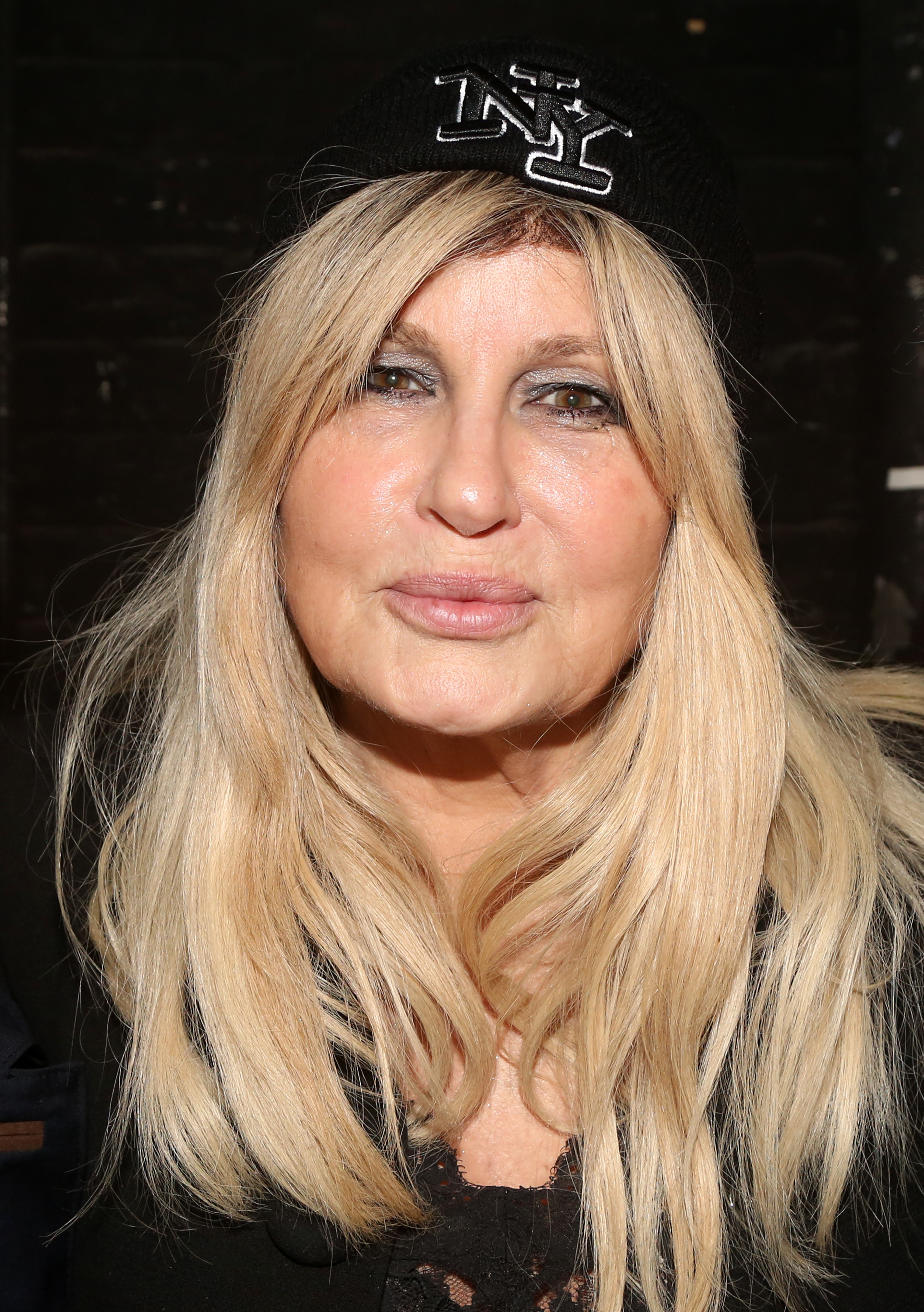 A woman wearing a beanie with "NY" lettering and a black outfit poses for a portrait