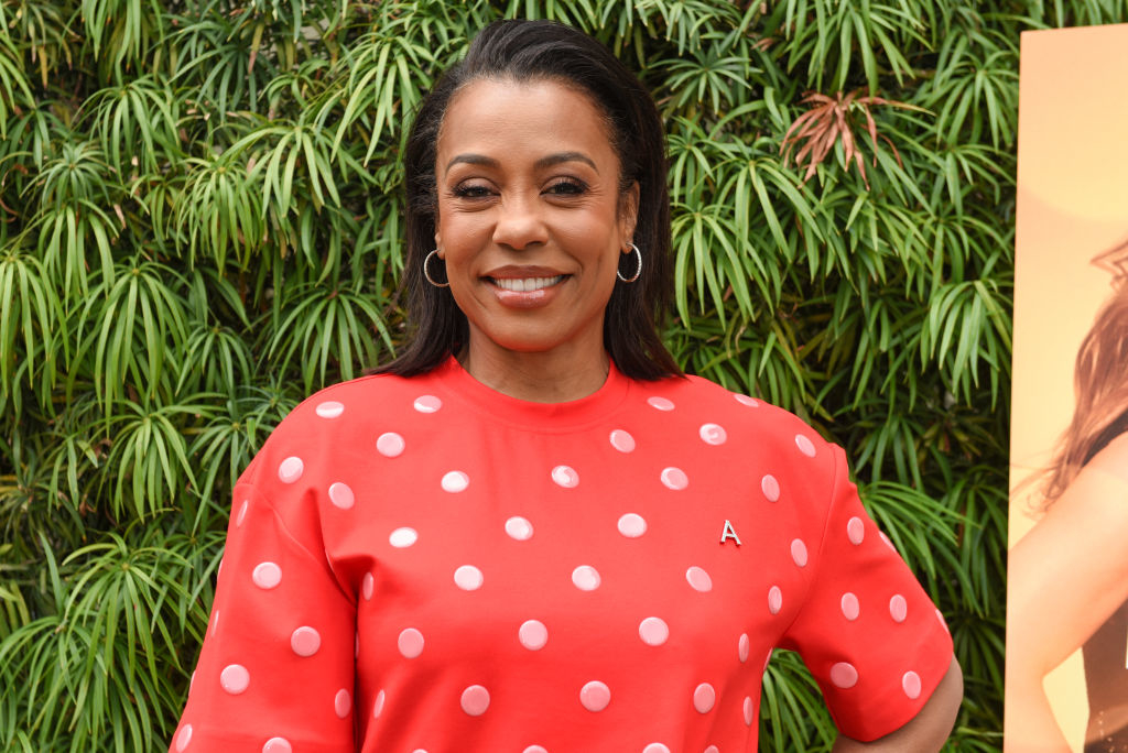 Woman wearing a polka dot shirt smiles in front of foliage