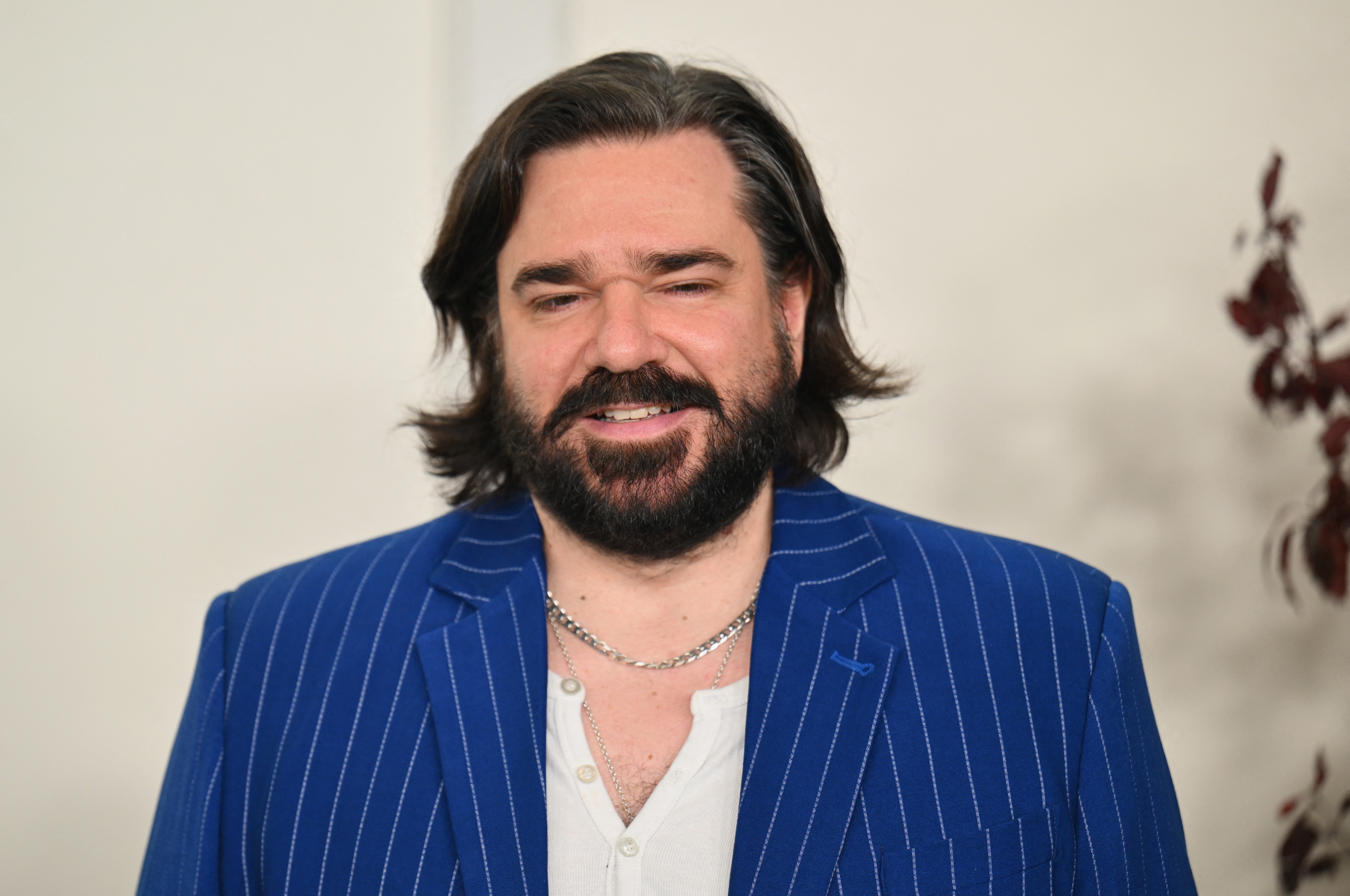 Matt Berry in a pinstriped suit jacket and white shirt, smiling at an event