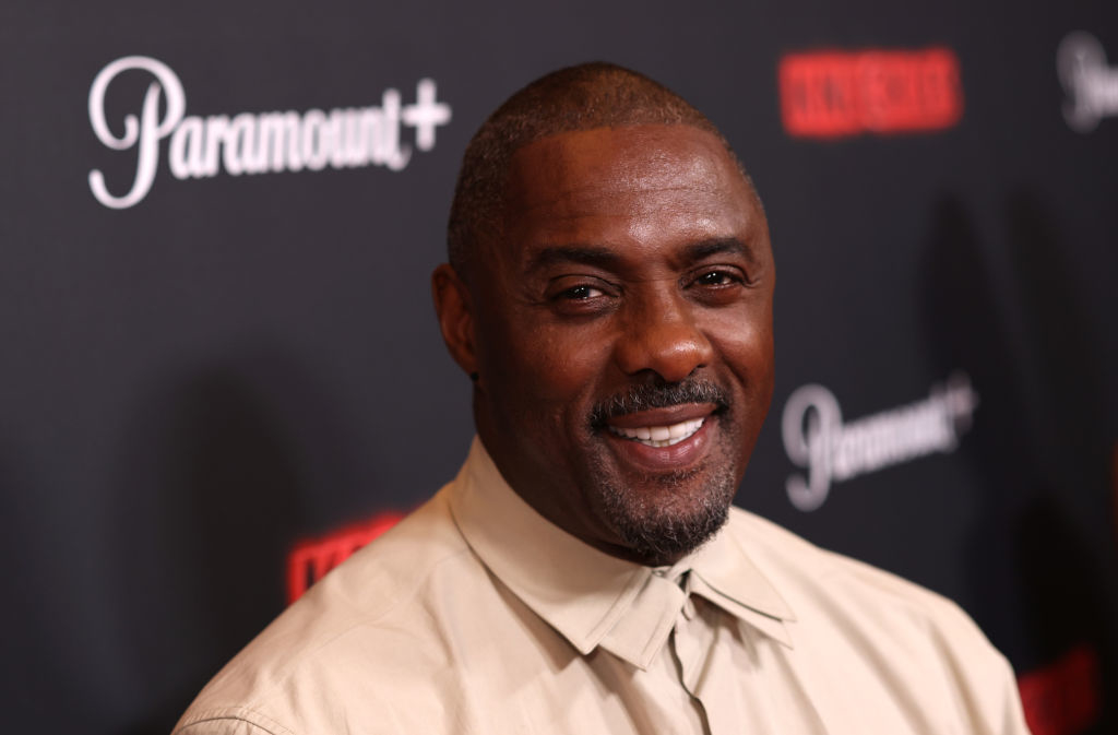 Idris Elba smiling at a Paramount+ event, wearing a beige collared shirt