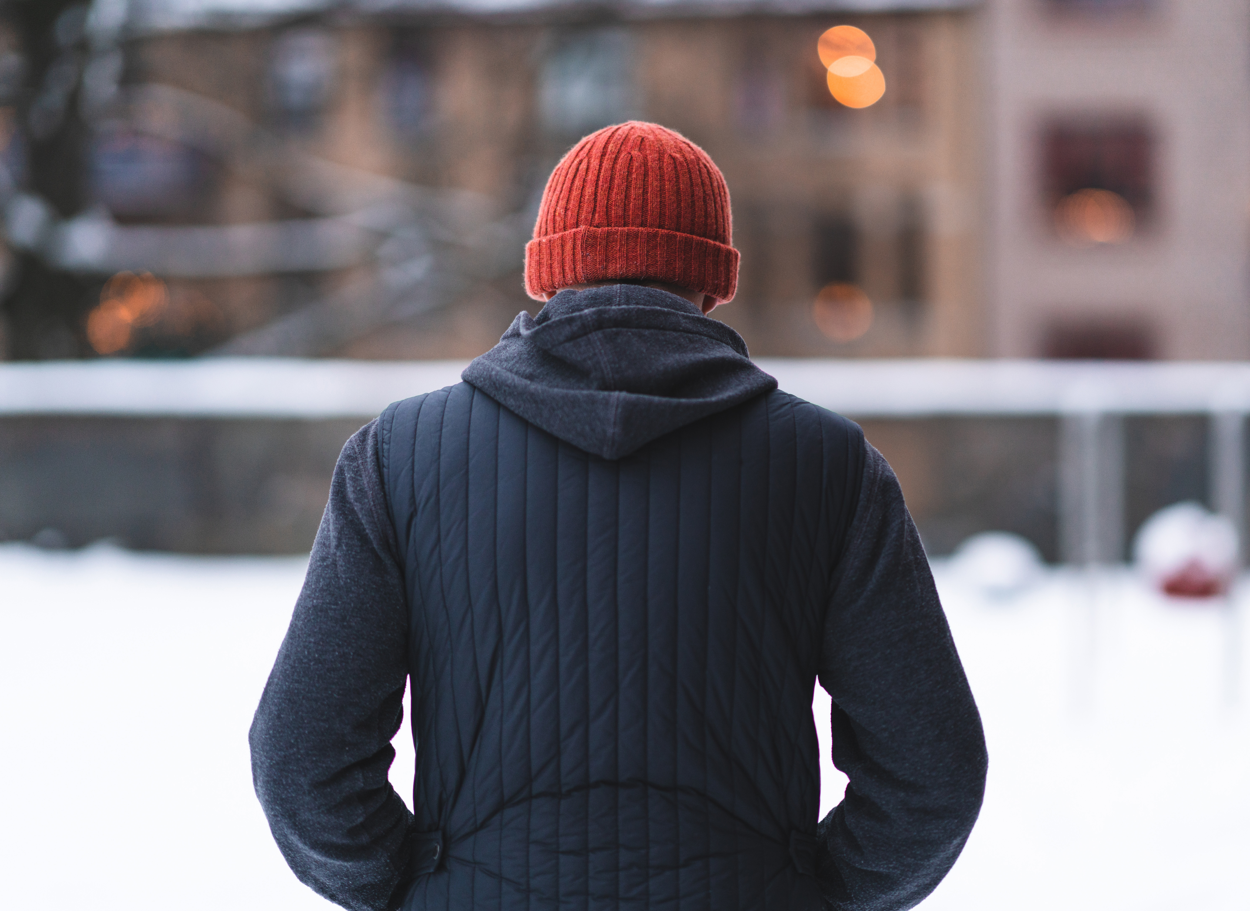 A person in a beanie and winter jacket stands with their back to the camera in a snowy outdoor setting