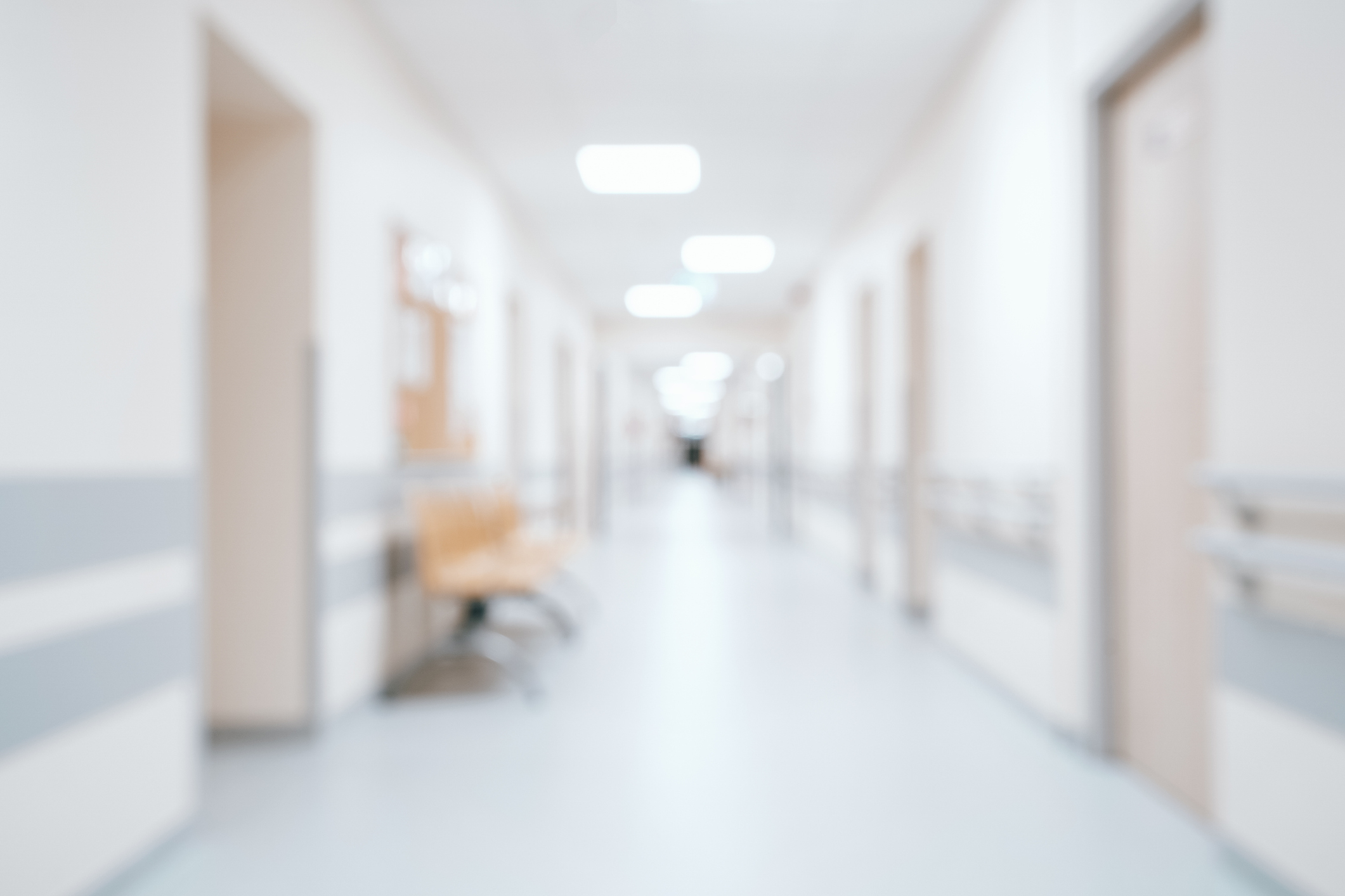 Blurred image of a hospital hallway with empty chairs against the wall and doors on either side