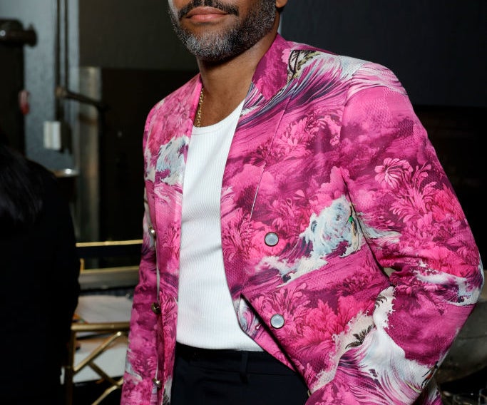 Donald Glover wearing a white shirt under a vibrant, patterned blazer, standing in an elegantly decorated room