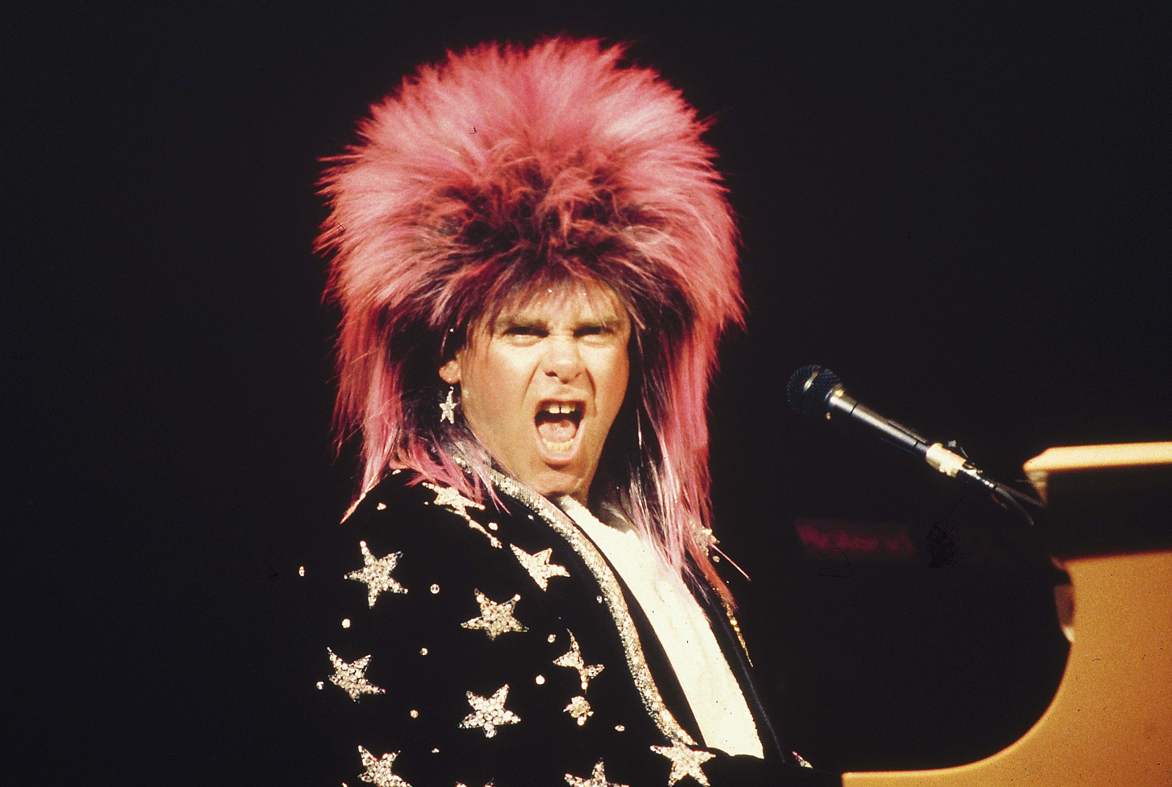 Elton John performing in a star-patterned coat, wearing a wig with spiky hair