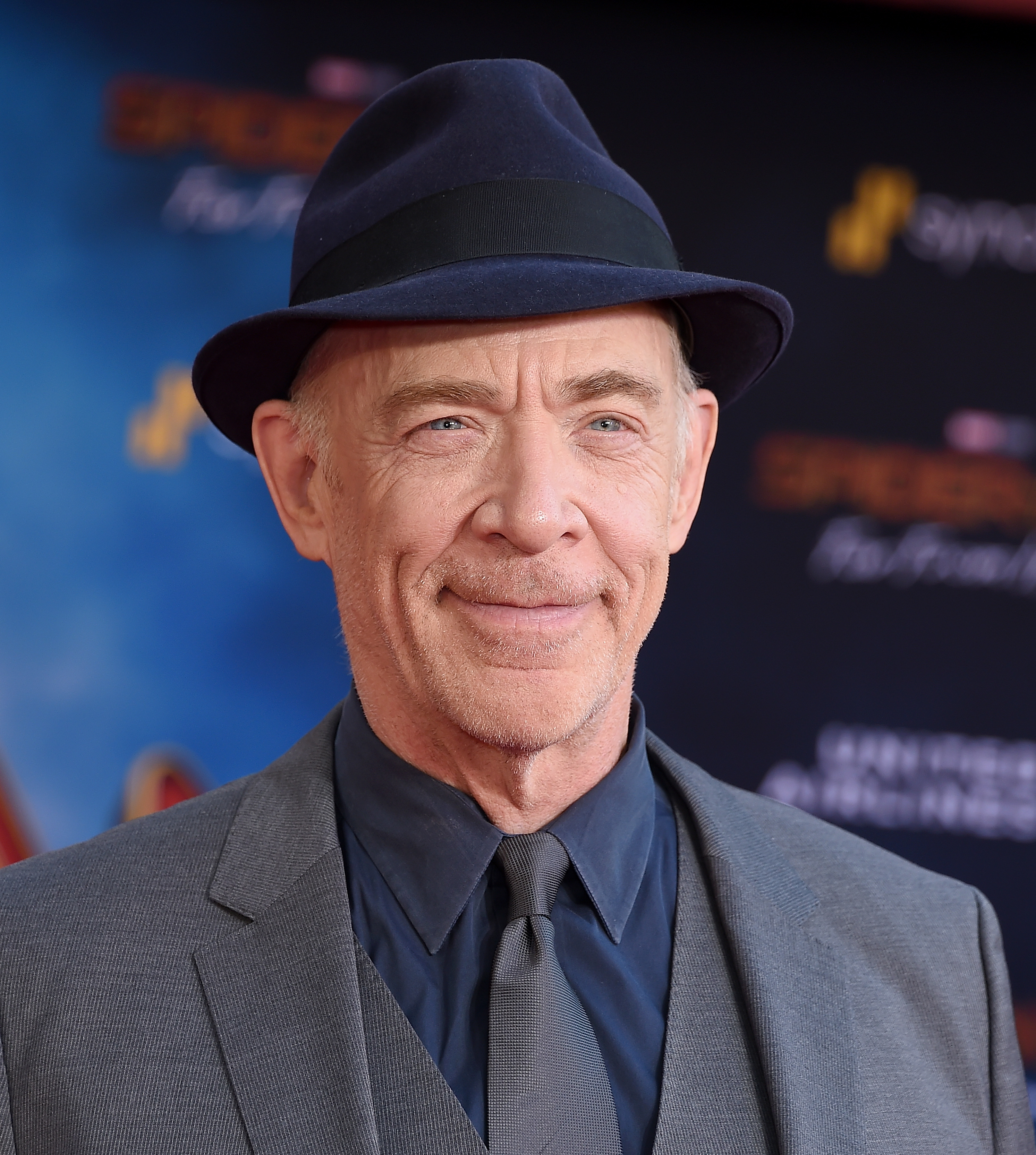 J.K. Simmons at a Spider-Man red carpet event, wearing a classic suit and tie with a fedora