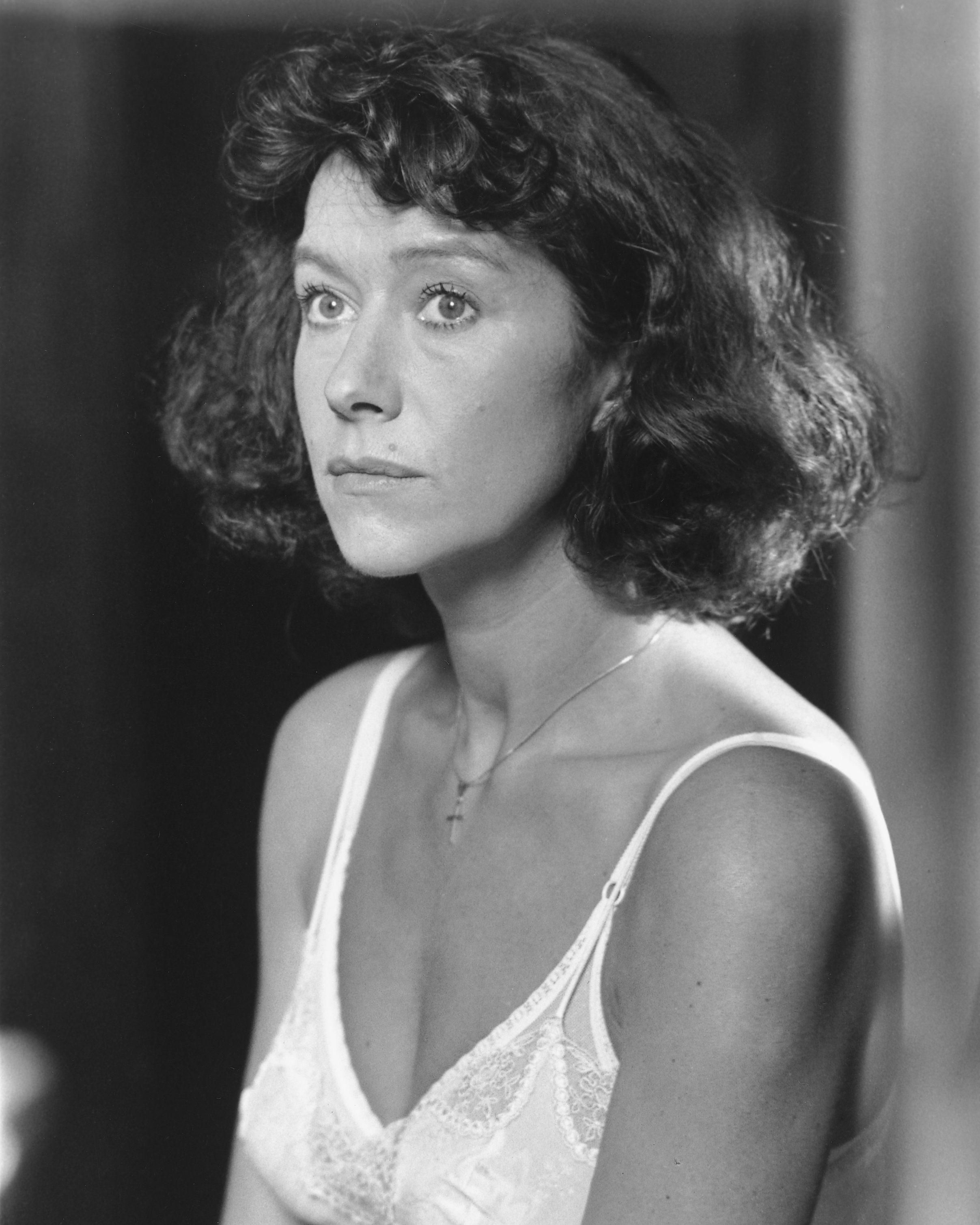 Woman with curly hair wearing a lace camisole, looking pensively