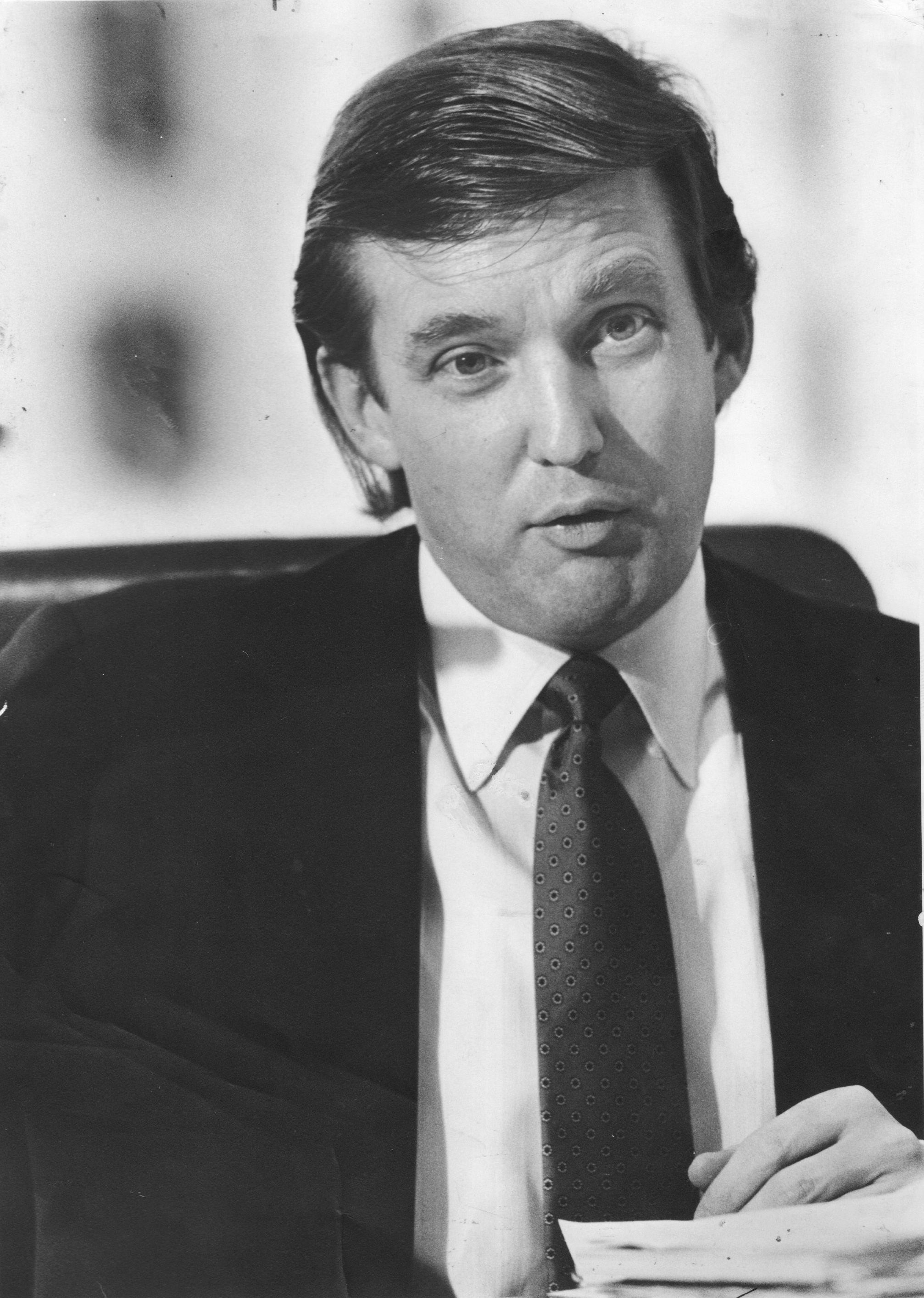 Donald Trump wearing a suit and tie, seated, and speaking or attending a meeting