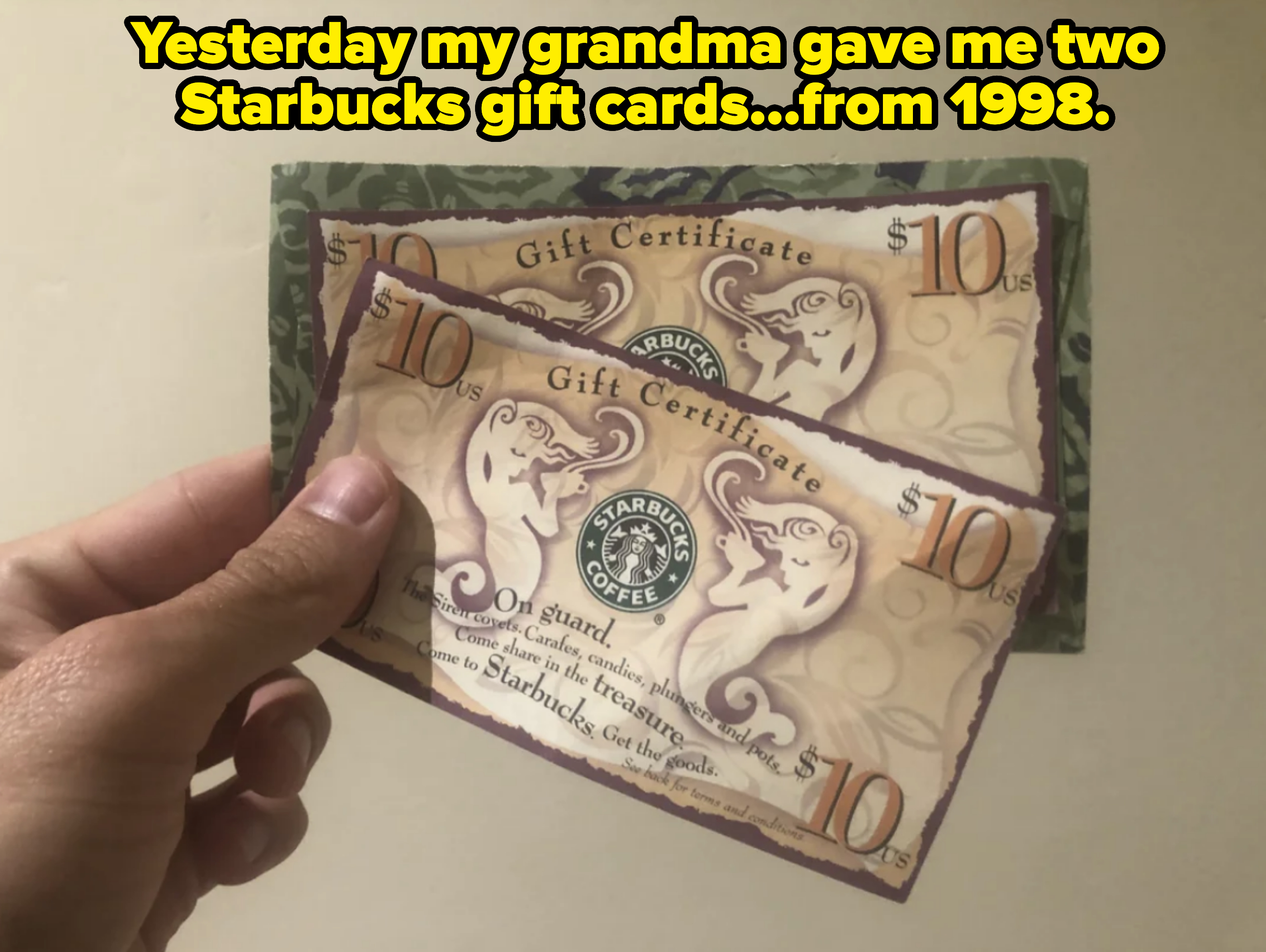 A hand holding two $10 Starbucks gift certificates