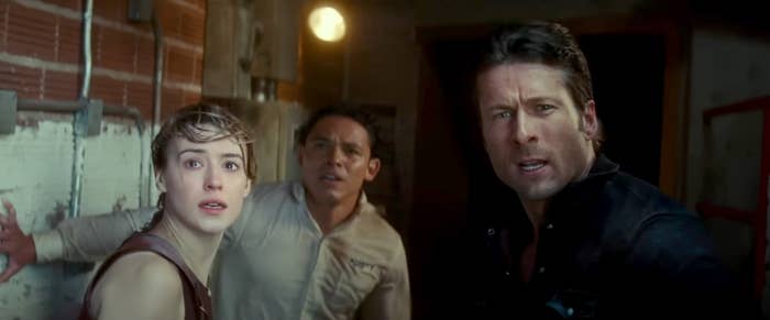 Daisy Edgar-Jones, Anthony Ramos, and Glen Powell looking distressed in a scene from a movie, standing in a dimly lit room with brick and concrete walls