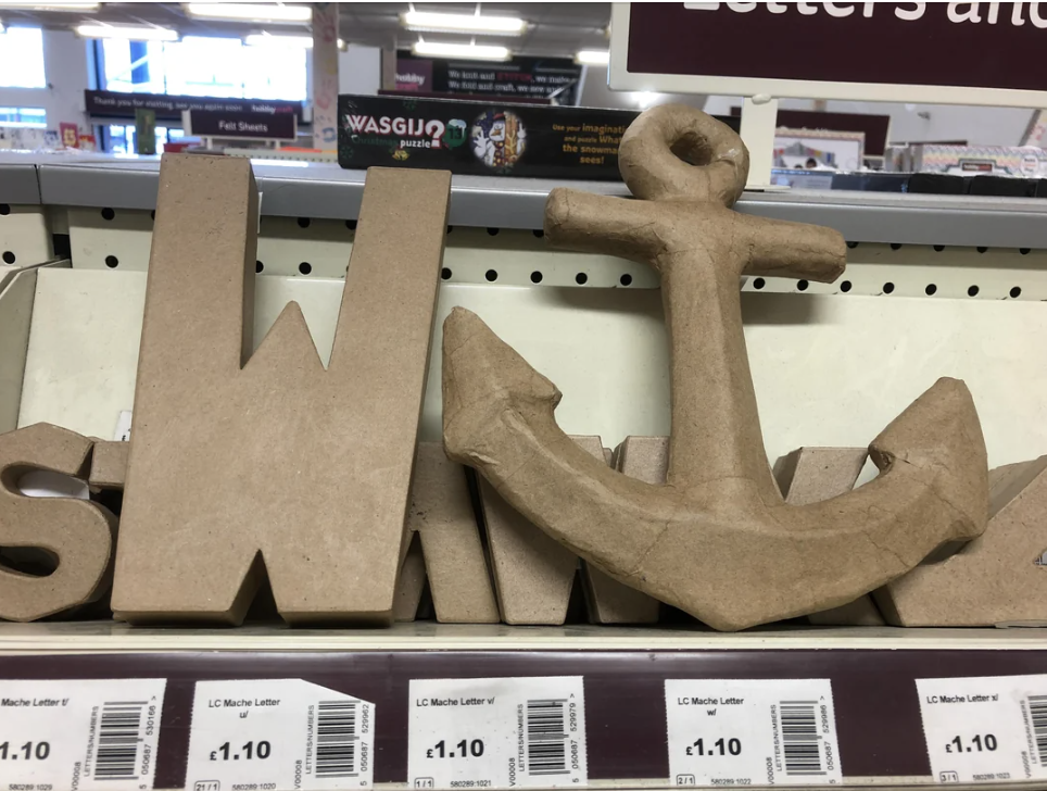 Cardboard letters and a decorative anchor displayed on a store shelf with price tags visible below each item