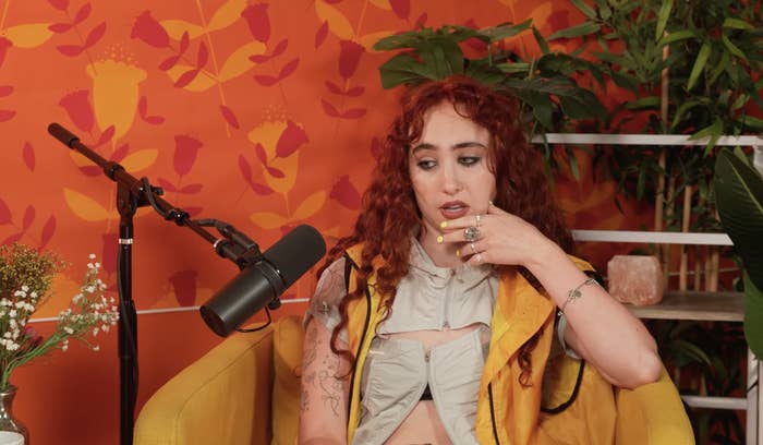 Chappell Roan sits in a yellow chair with a microphone nearby, wearing a sleeveless top with tattoos visible on her arms