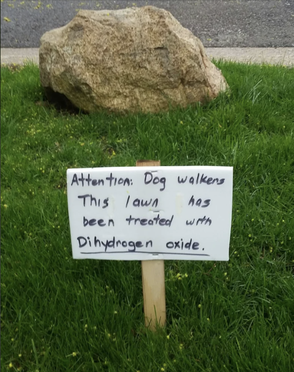 A sign on a lawn reads, "Attention: Dog walkers. This lawn has been treated with Dihydrogen oxide."