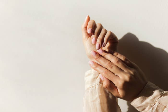 A close-up image of a person's well-groomed hands with neatly trimmed and manicured nails placed against a plain background