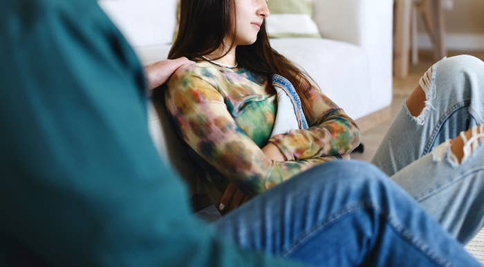 Father and daughter on a couch in a living room; the daughter is looking away with an upset expression