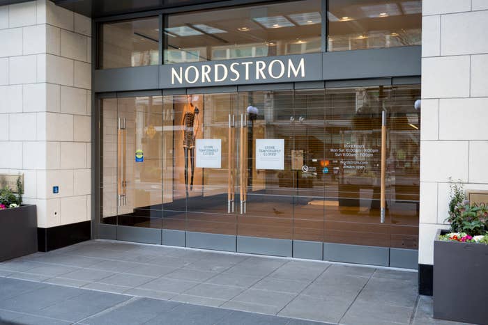 The image shows the entrance of a Nordstrom store with glass doors and a sign above reading &quot;Nordstrom.&quot; There are two potted plants outside near the entrance