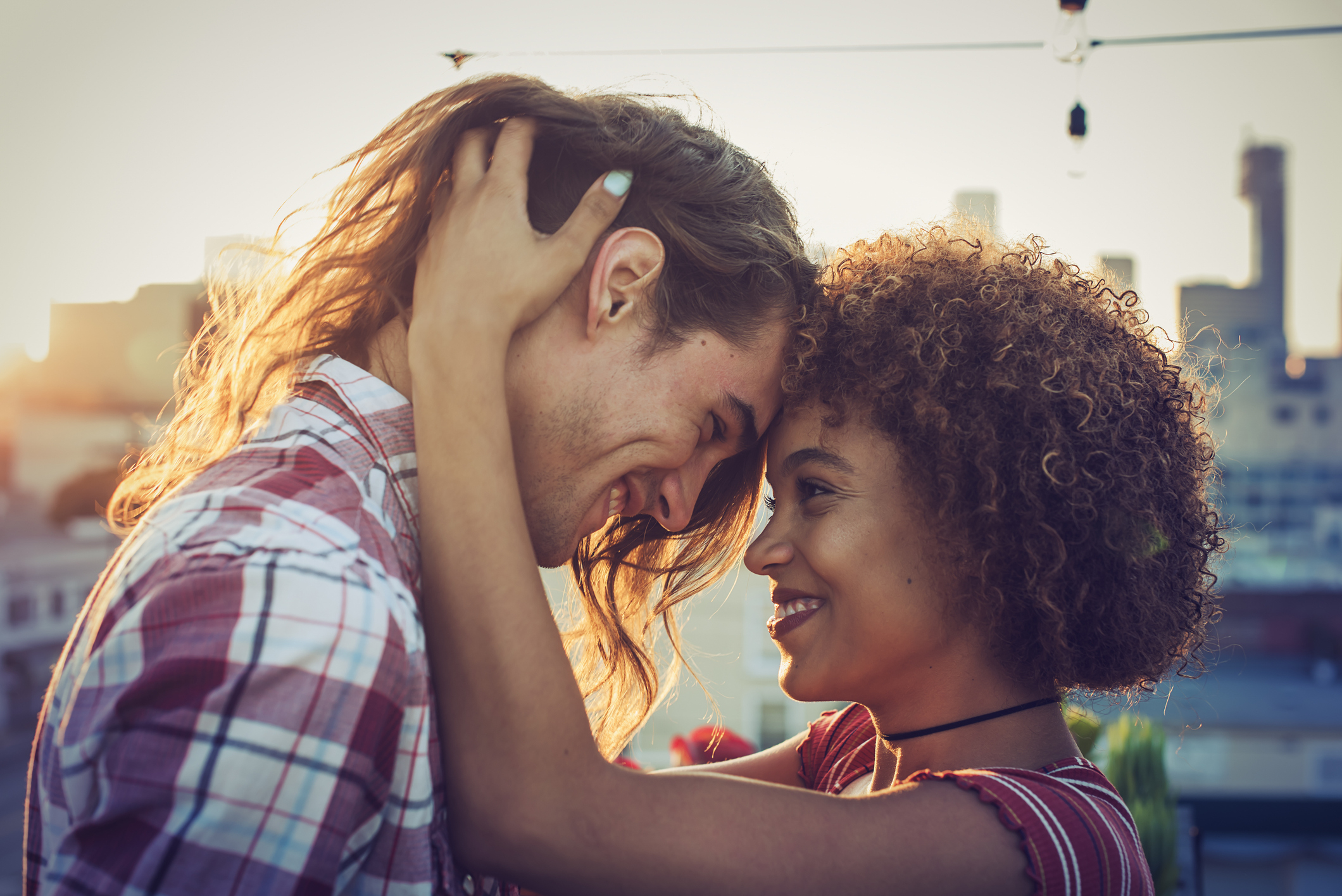 Two people sharing an affectionate moment, heads touching, with a cityscape in the background