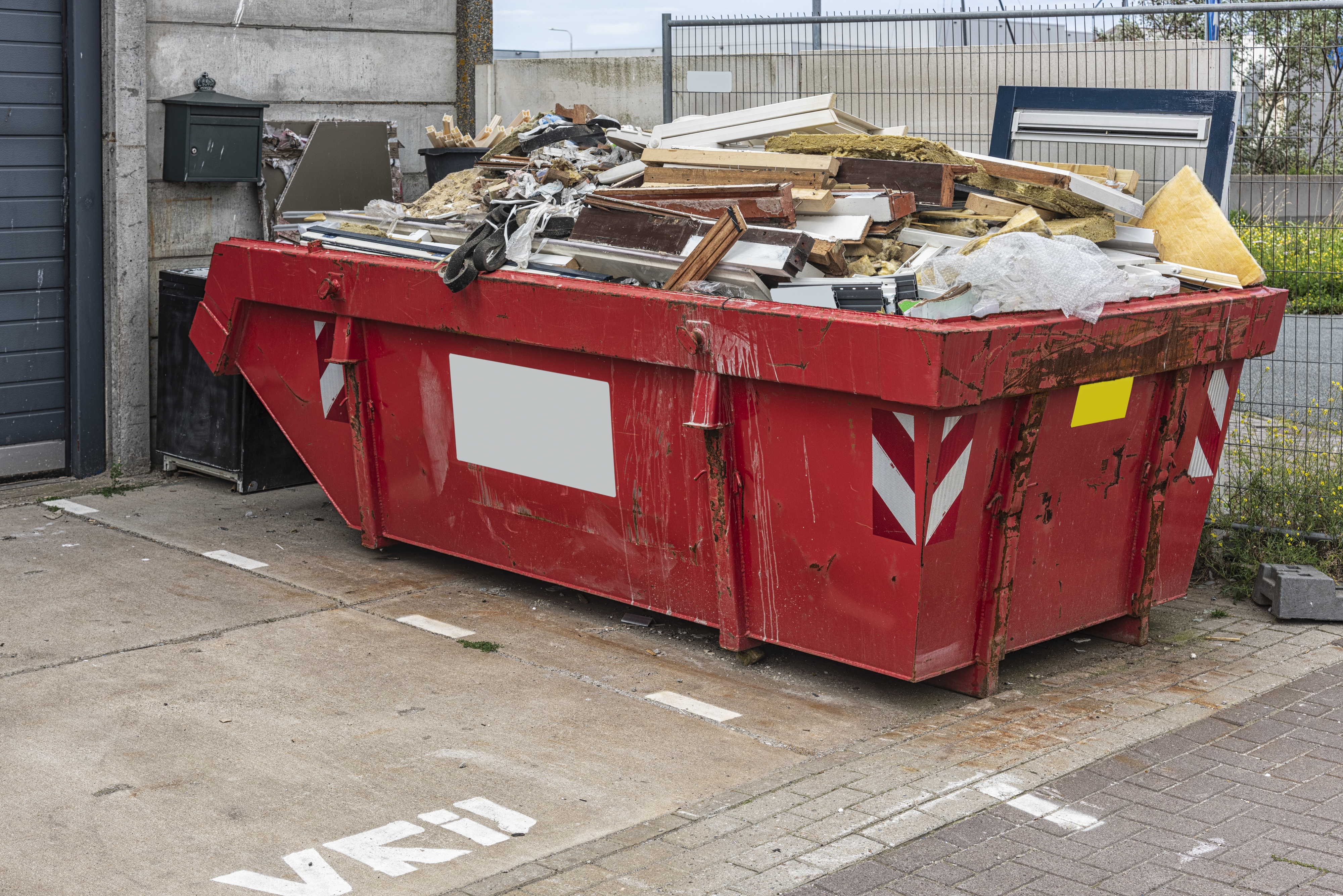 A large red dumpster overflowing with construction debris, set in an outdoor area near a building