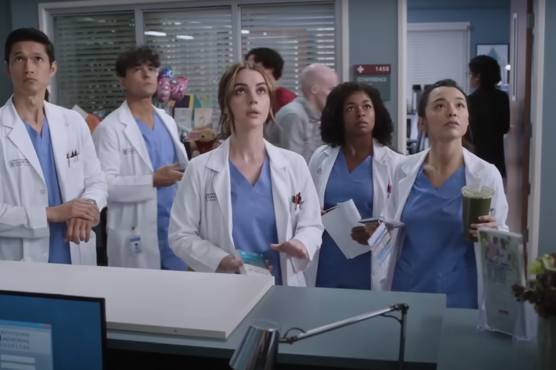 Doctors in scrubs, including five individuals, are looking up in a medical facility